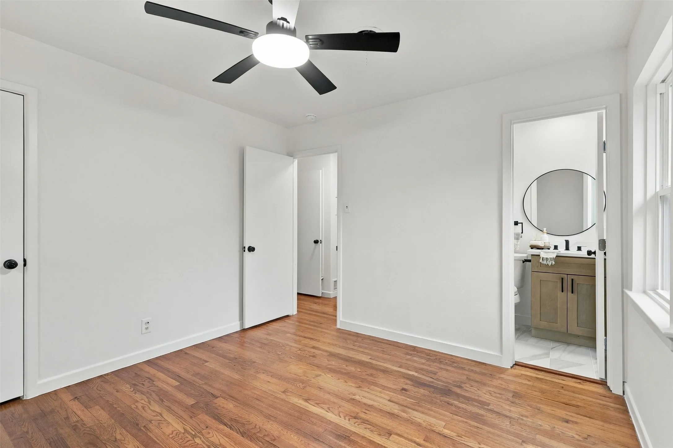 Wood-finish flooring, ceiling fan with integrated lighting, white walls, and white trim