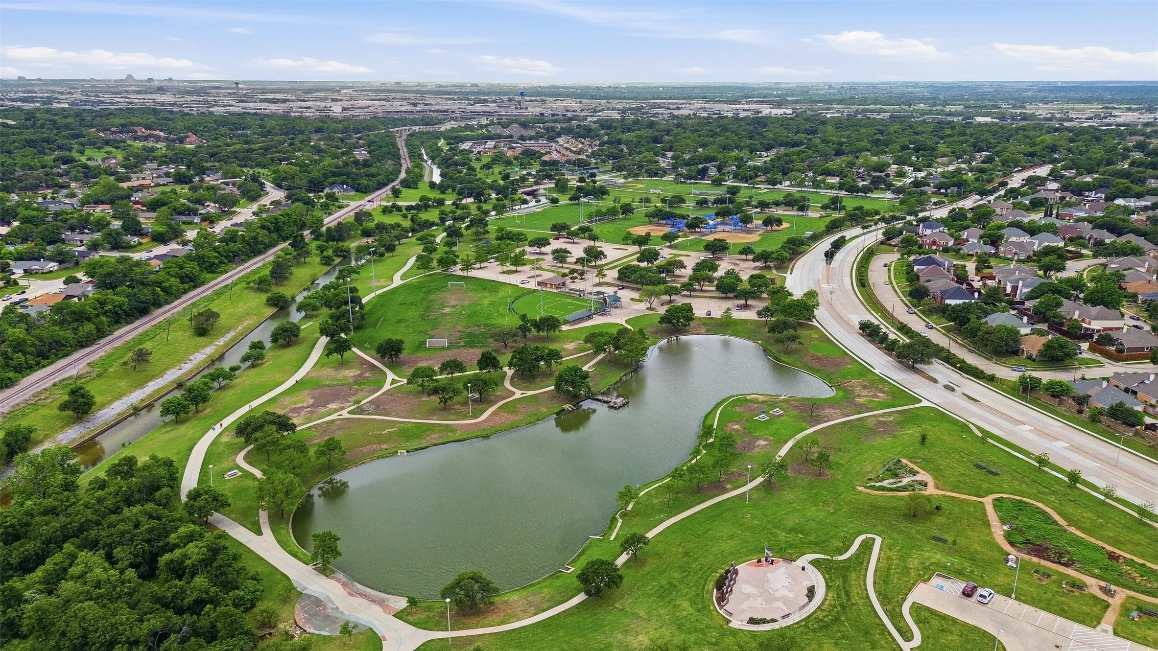Expansive green spaces with a central pond, paved walking paths, and mature trees