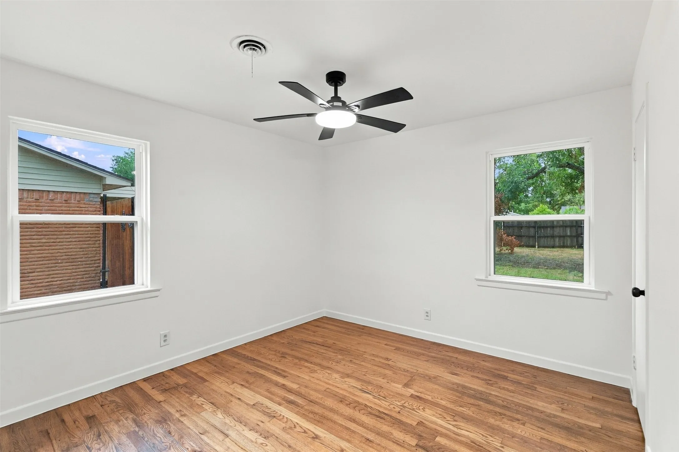 Wood-finish flooring, white walls, two windows, ceiling fan with integrated lighting