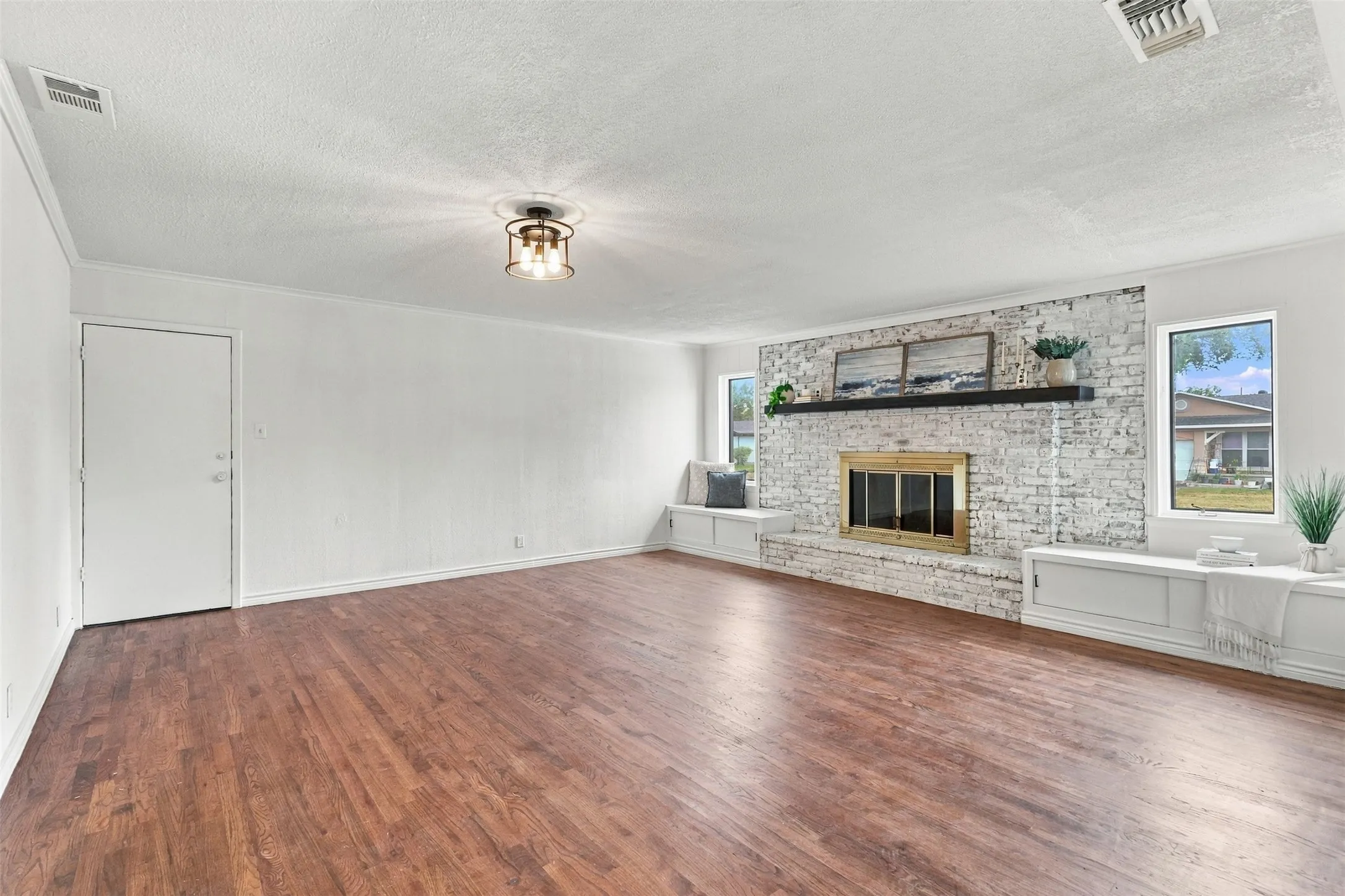 Wood-finish flooring, white brick fireplace with a brass-finish insert, black mantel, built-in bench seating, and a flush-mount ceiling light fixture