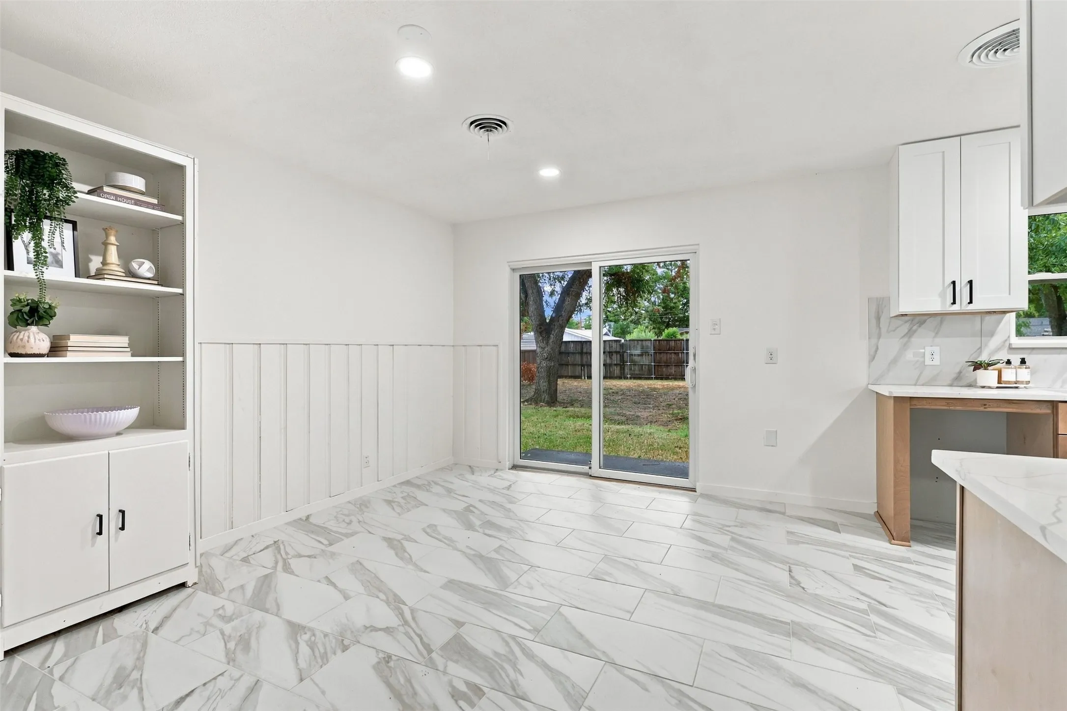 White cabinetry, built-in shelving, white shiplap wainscoting, sliding glass door, and large format tile flooring