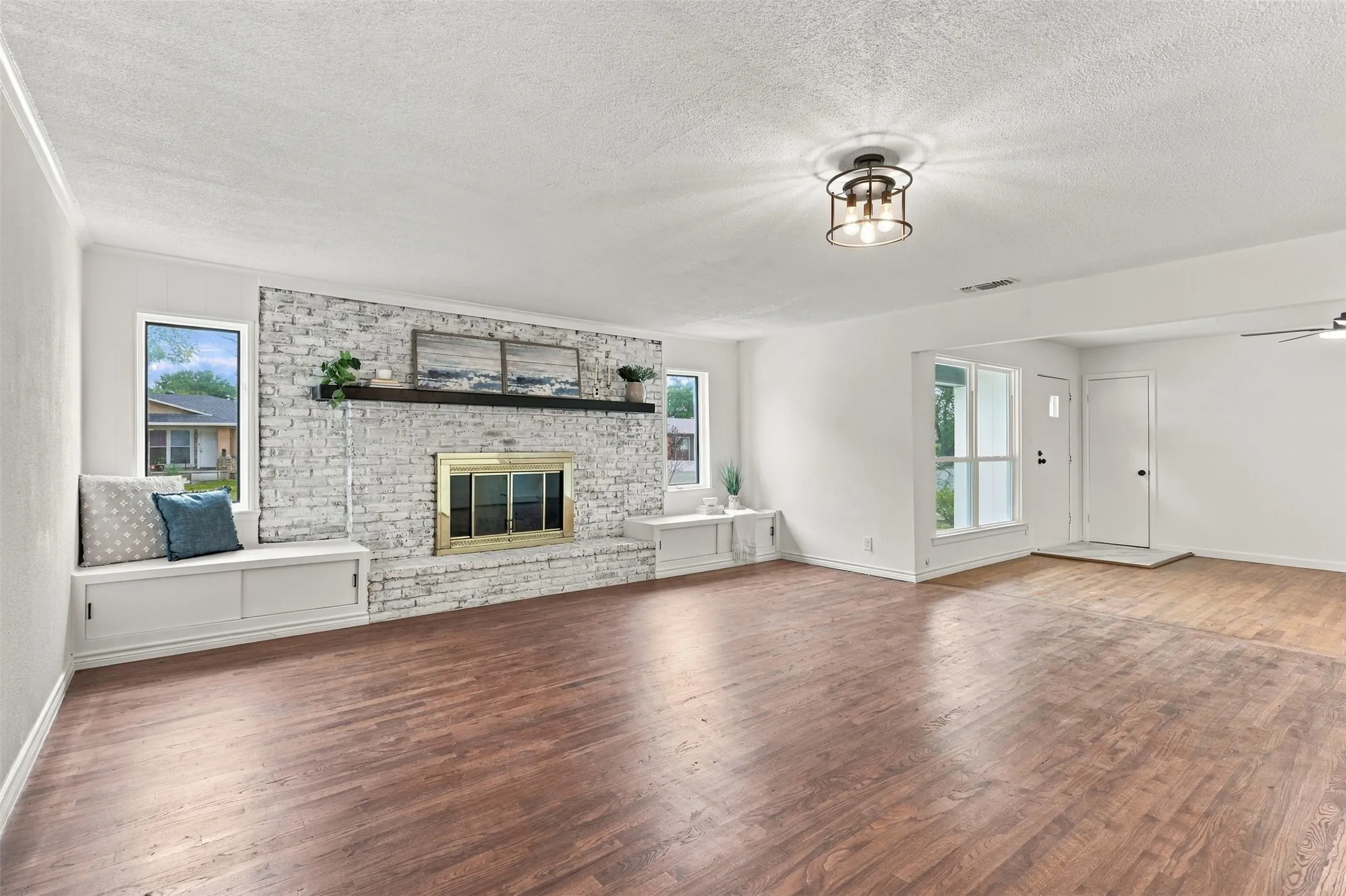 Expansive living area featuring wood-finish flooring, a white brick fireplace with a wood mantle, and built-in window seating with storage