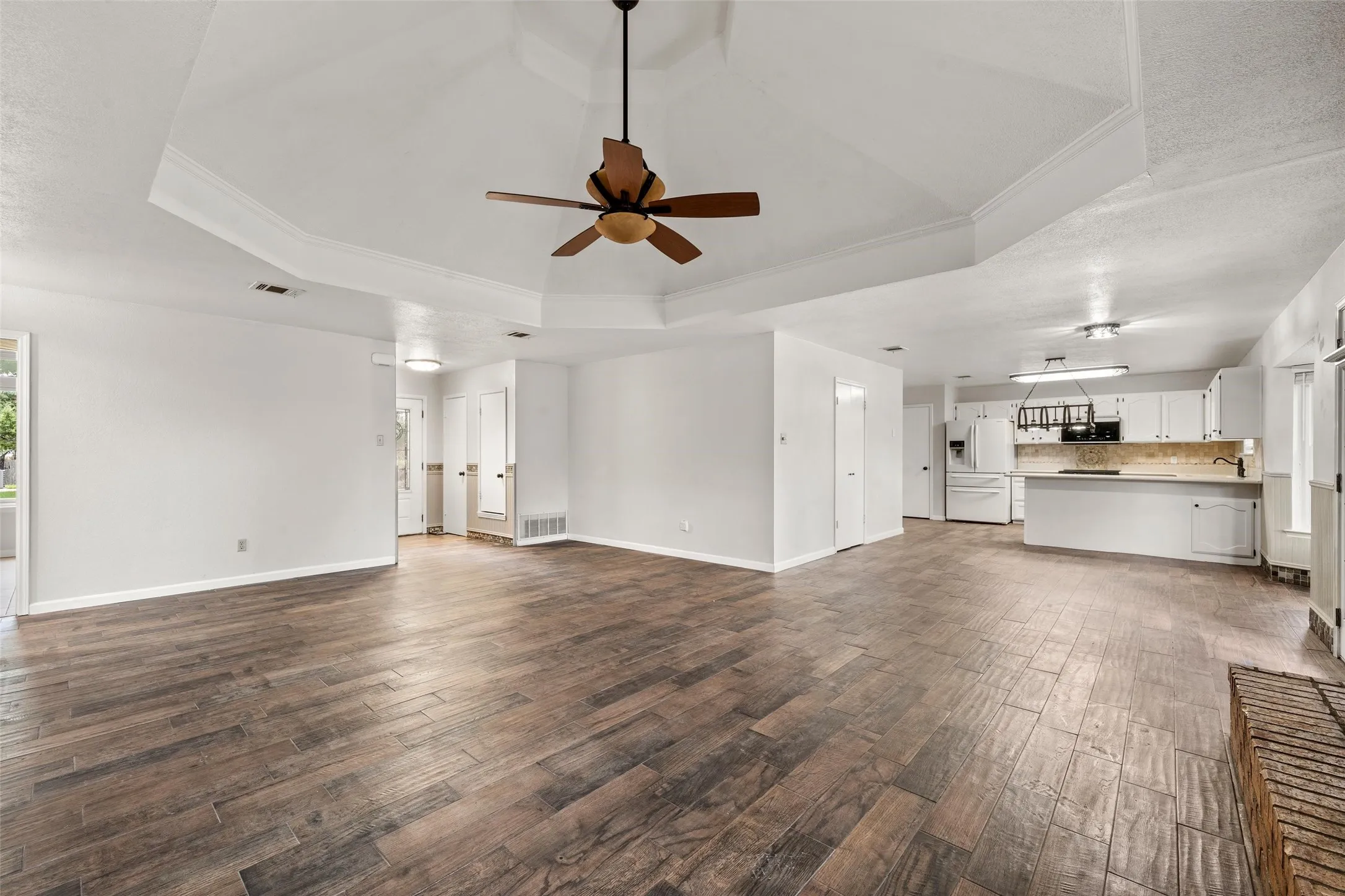 Open-concept living space featuring a tray ceiling, wood-finish flooring, and a ceiling fan