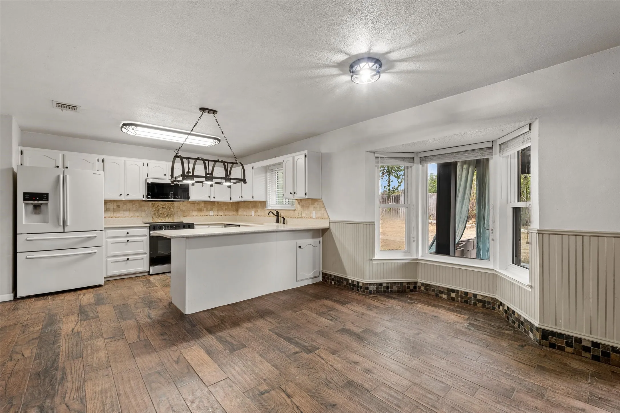 Kitchen featuring wood-finish flooring, white cabinetry, a built-in oven, and a bay window