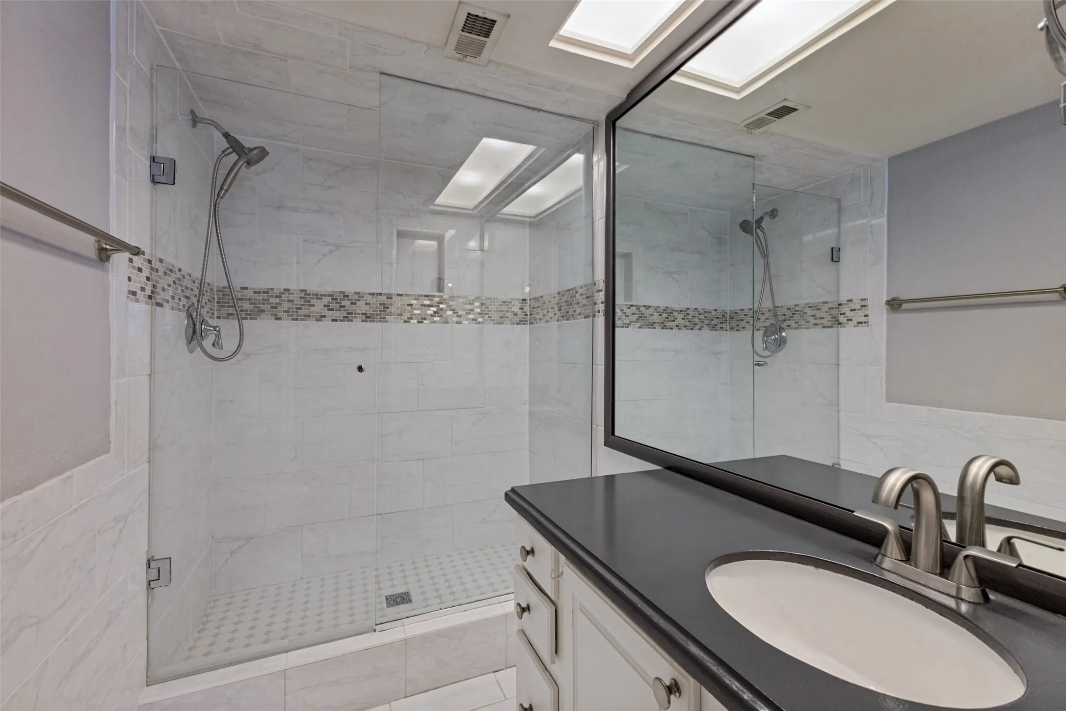 Glass-enclosed shower with white tiled walls and mosaic accent