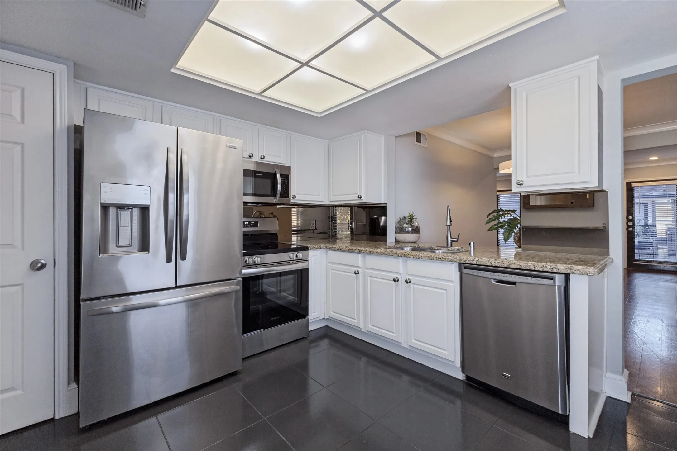 Kitchen featuring white cabinetry, stainless steel appliances, granite countertops, and dark tile flooring