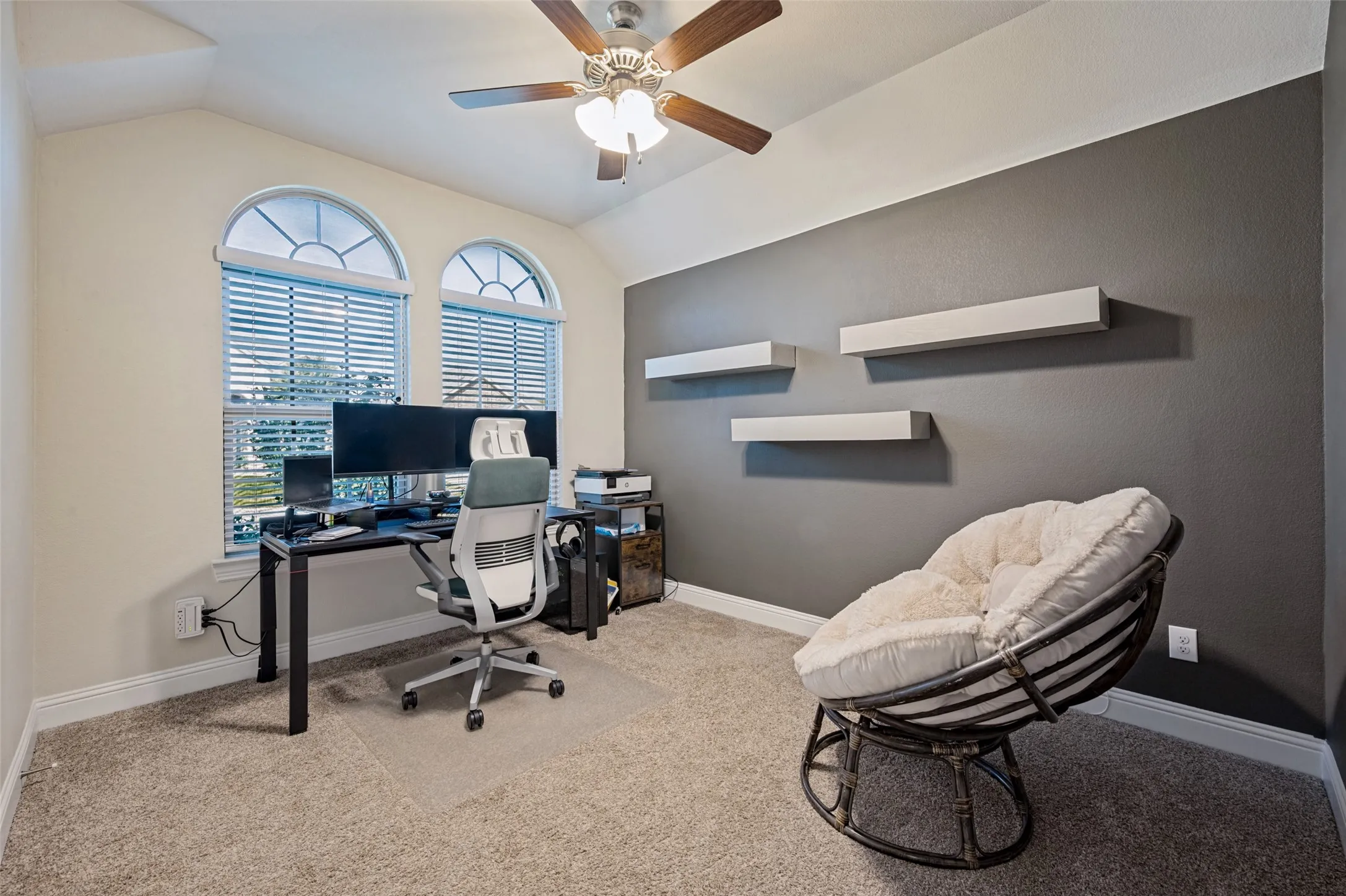 Arched windows with blinds, ceiling fan, carpeted flooring, and wall-mounted shelving