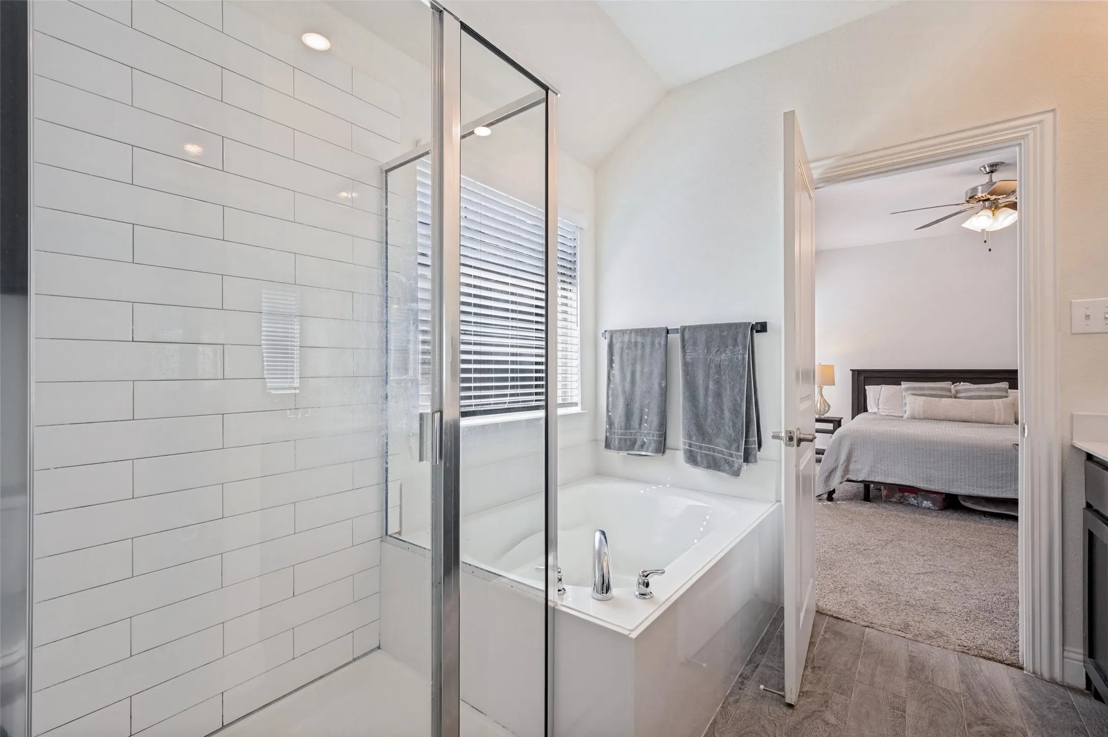 Glass-enclosed shower with subway tile surround, separate soaking tub with chrome fixtures, and wood-finish flooring