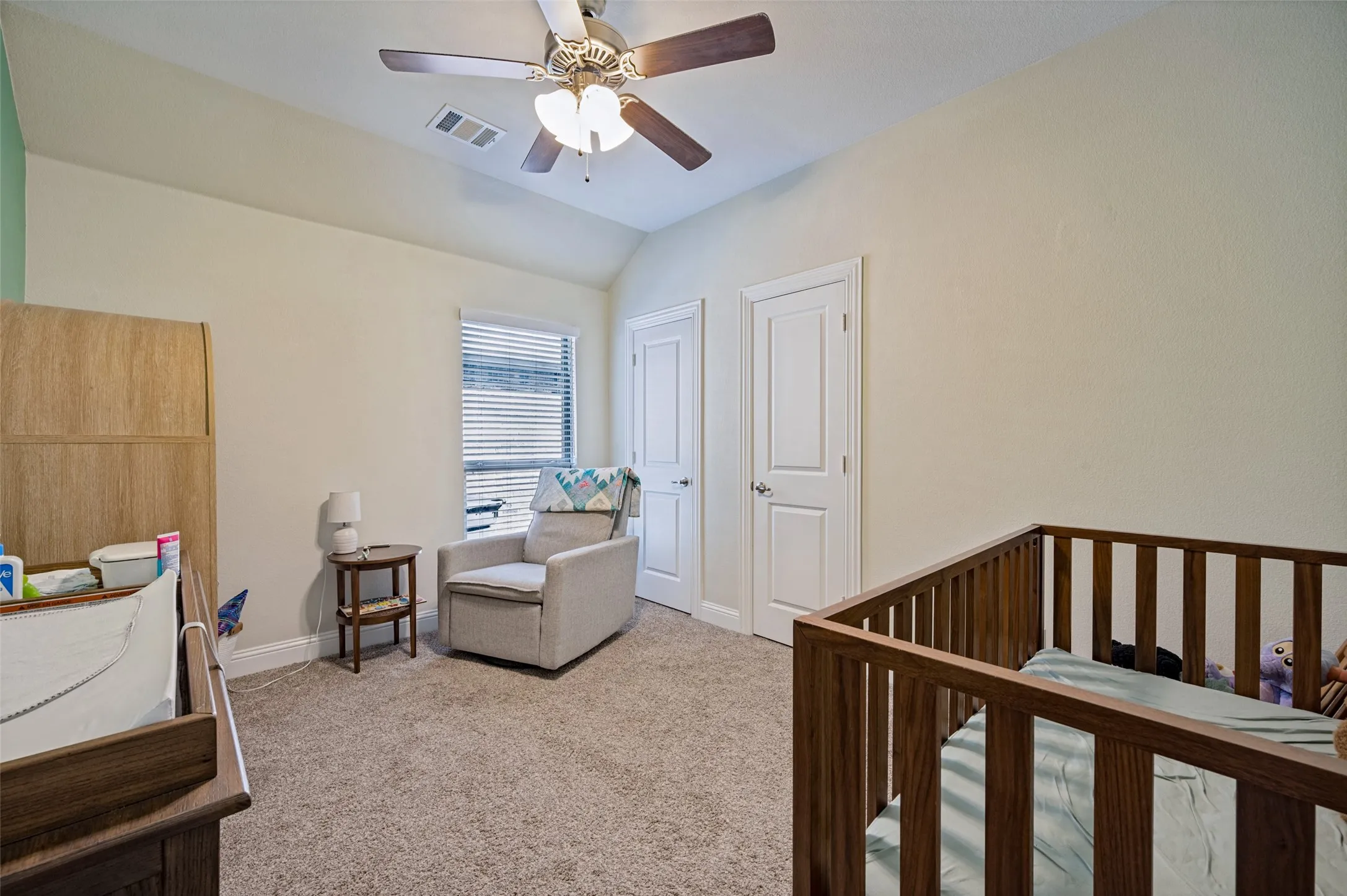Vaulted ceiling with a ceiling fan, window with blinds, two paneled doors, and carpeted flooring