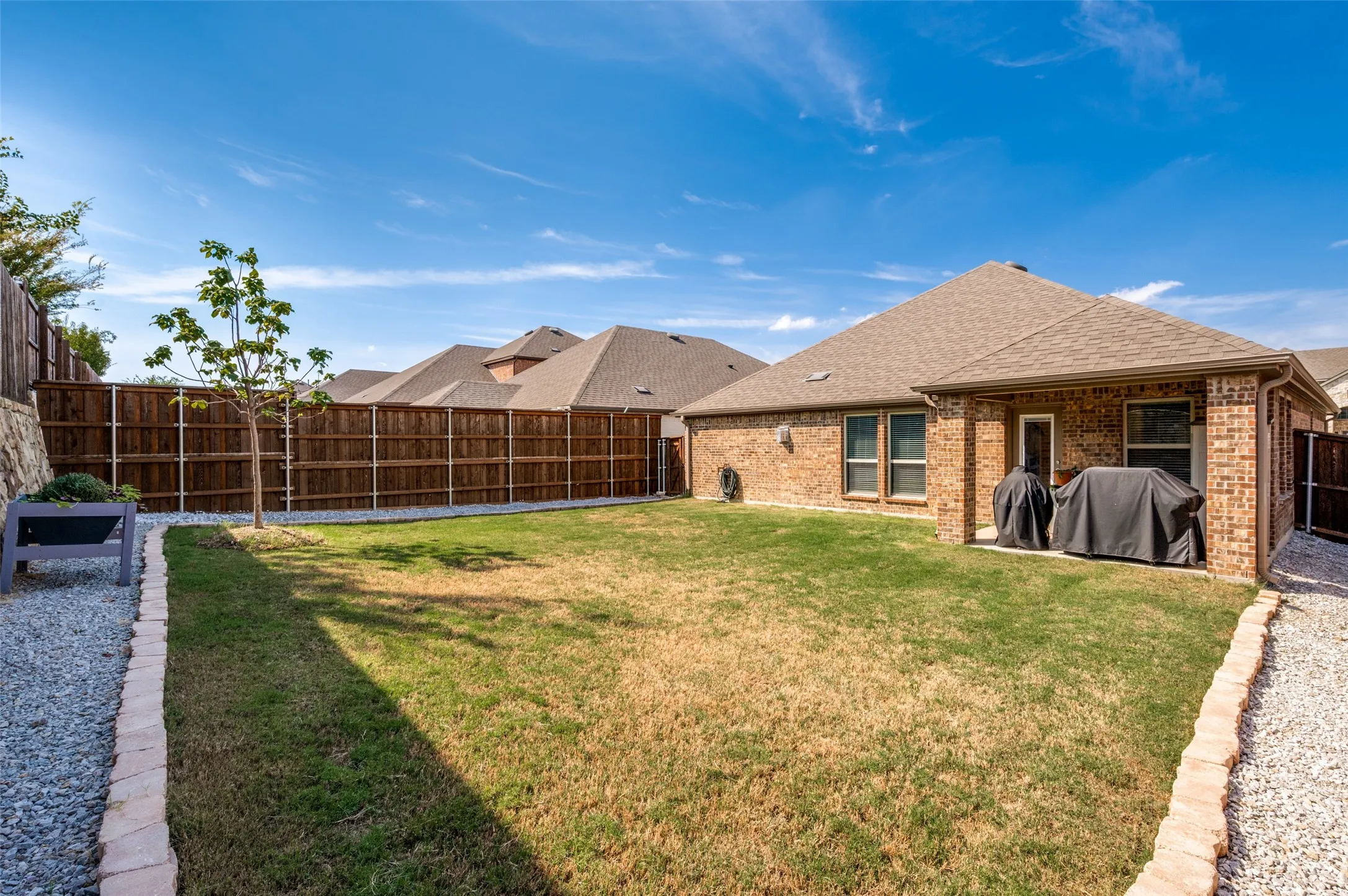 Expansive backyard featuring a manicured lawn, gravel perimeter, brick border, and privacy fencing