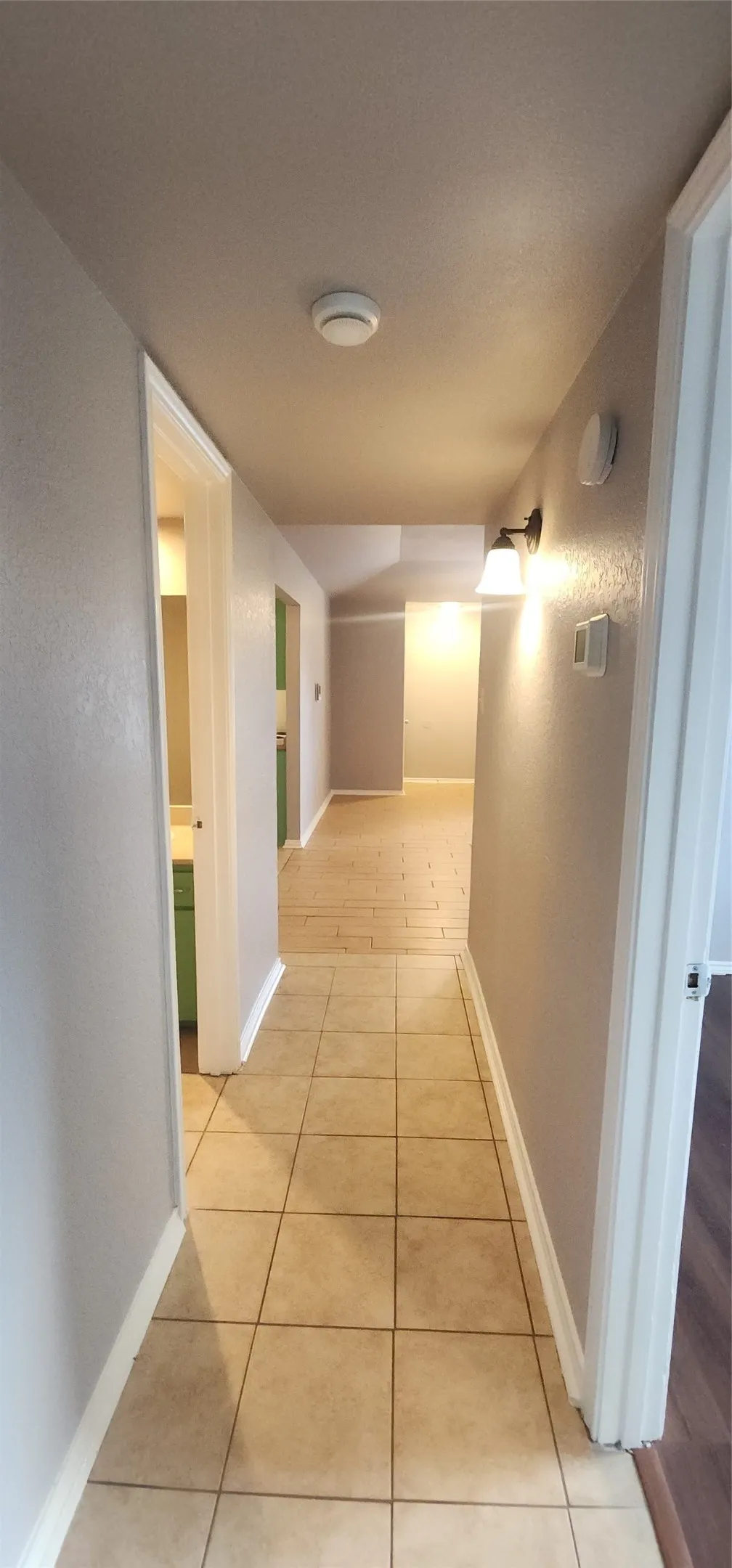 Hallway featuring ceramic tile flooring, light neutral wall color, and a wall-mounted light fixture