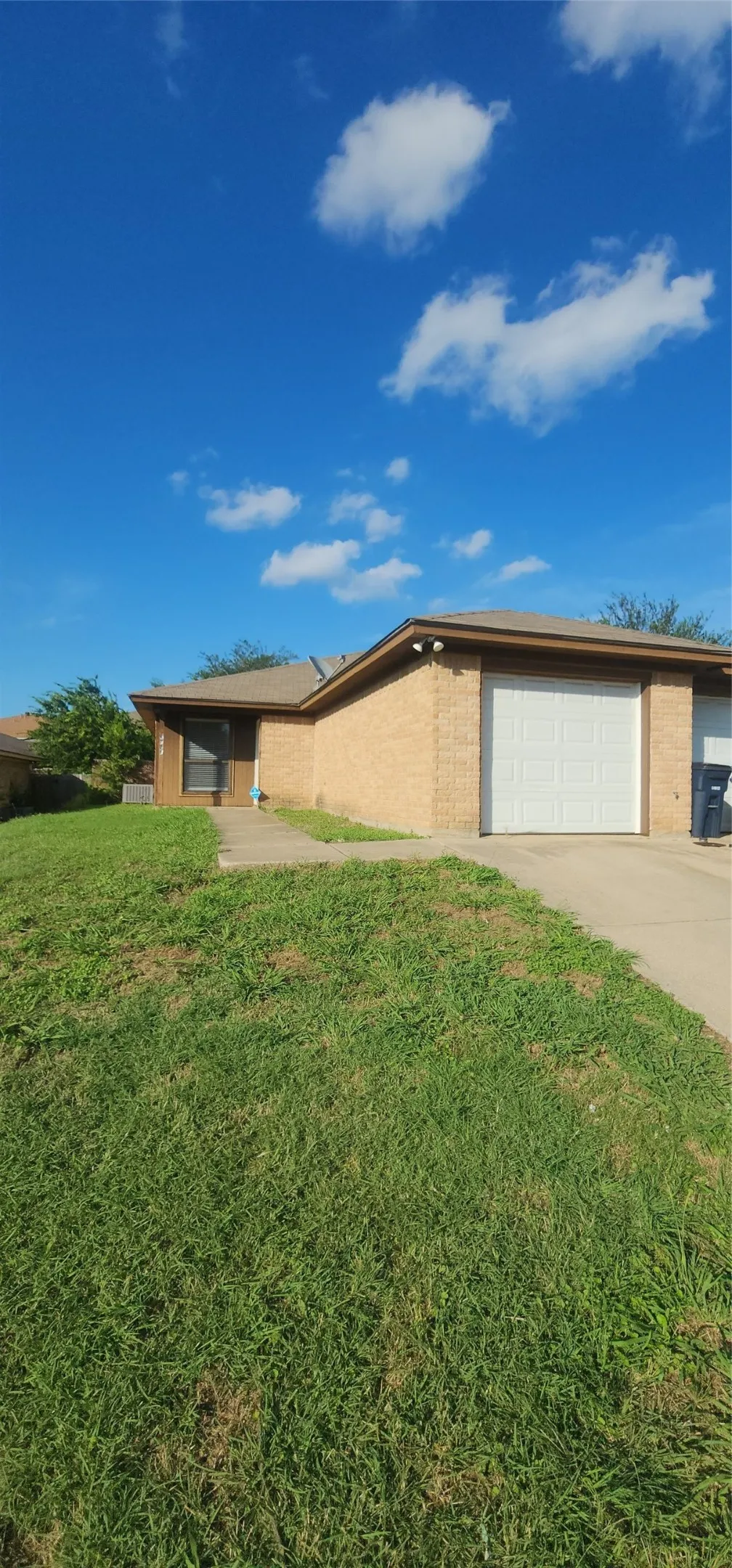 Brick exterior with a white garage door, concrete driveway, and a sloped front lawn