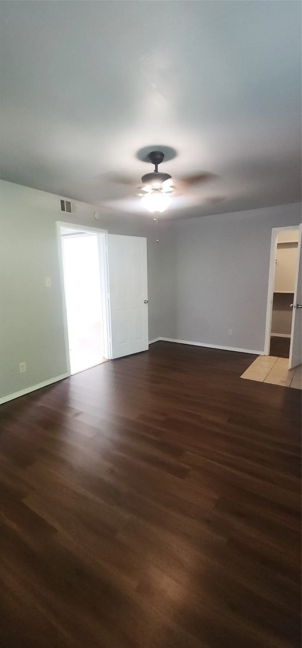 Dark wood-finish flooring with light gray wall paint and a ceiling fan