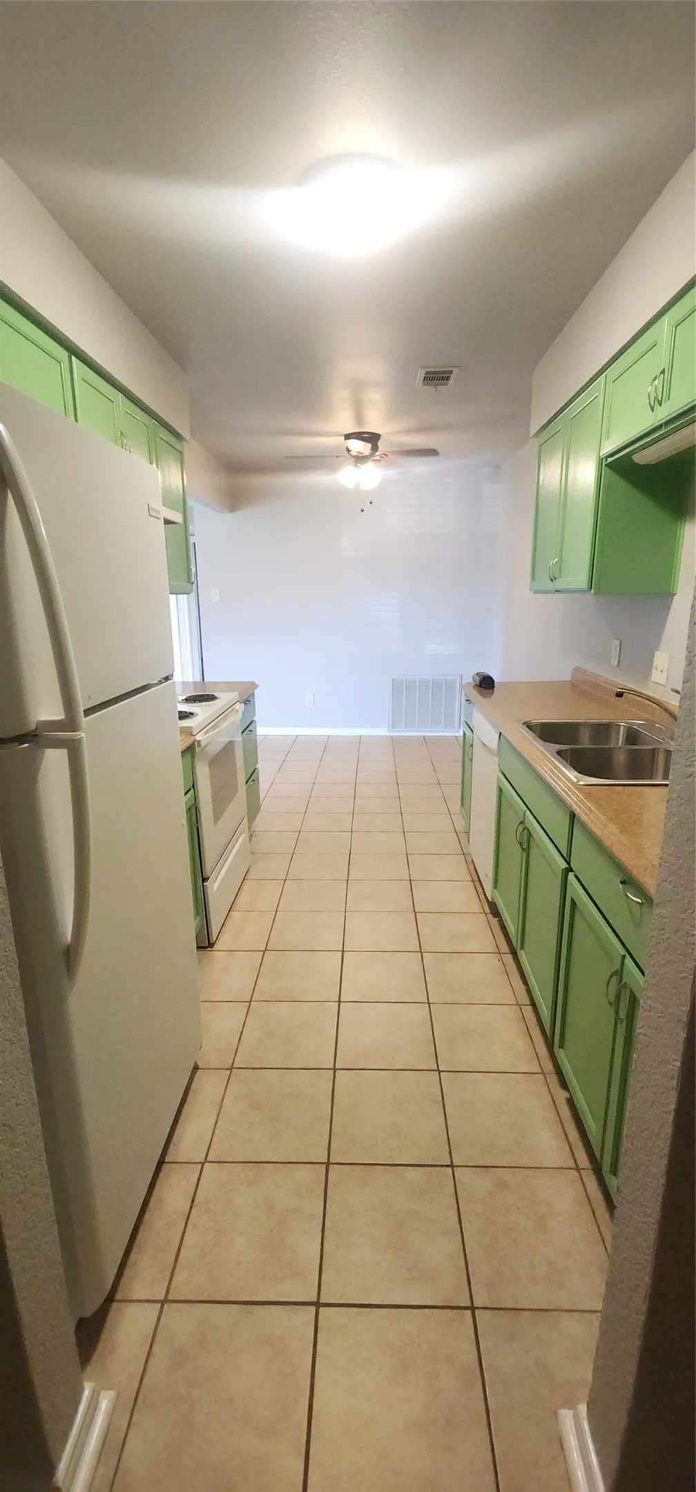 Galley kitchen featuring ceramic tile flooring, upper and lower cabinetry, a double basin sink, and a full suite of appliances