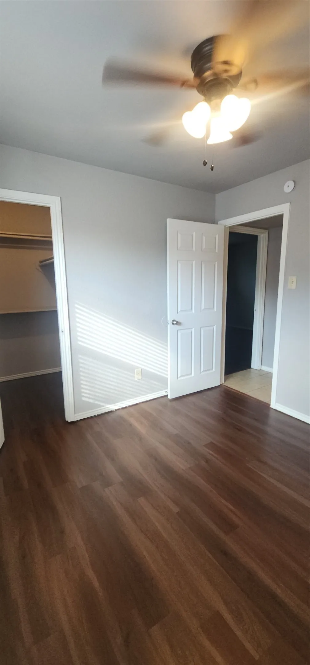 Wood-finish flooring, ceiling fan with integrated lighting, neutral wall tones, white trim, and built-in closet shelving