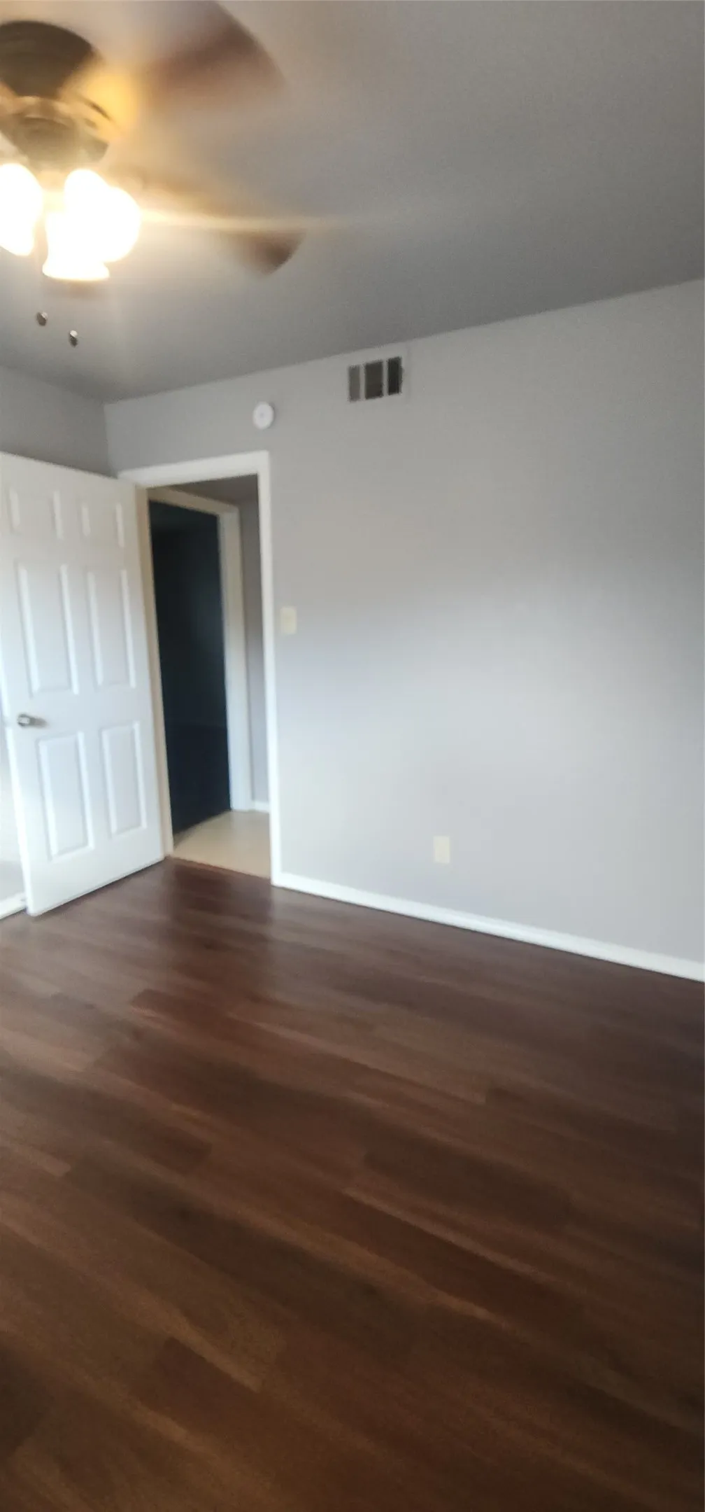 Wood-finish flooring, light gray wall paint, and a ceiling fan with integrated lighting