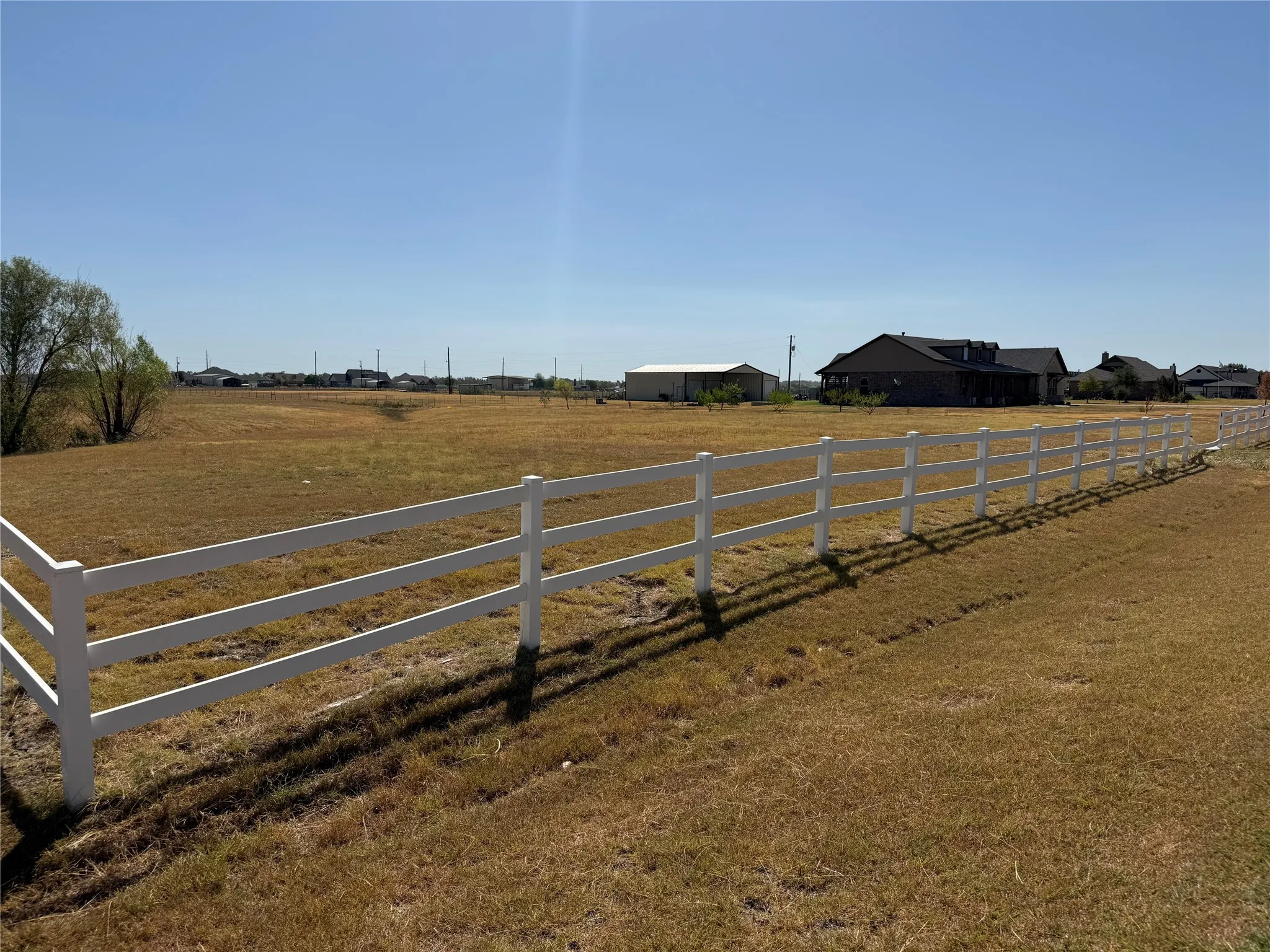 Expansive land parcel featuring a white three-rail fence and a backdrop of established properties