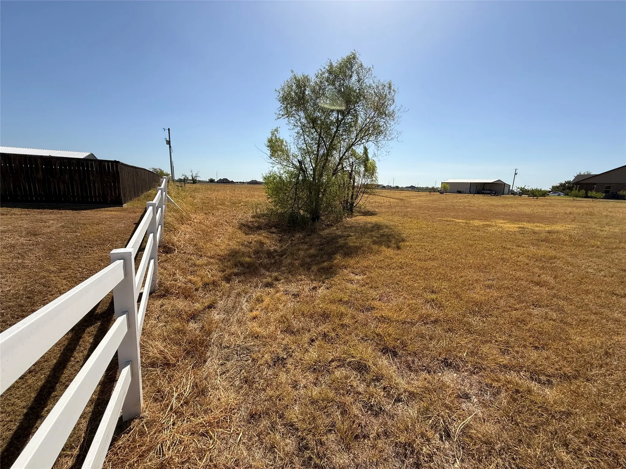 Expansive open lot featuring a white post-and-rail fence