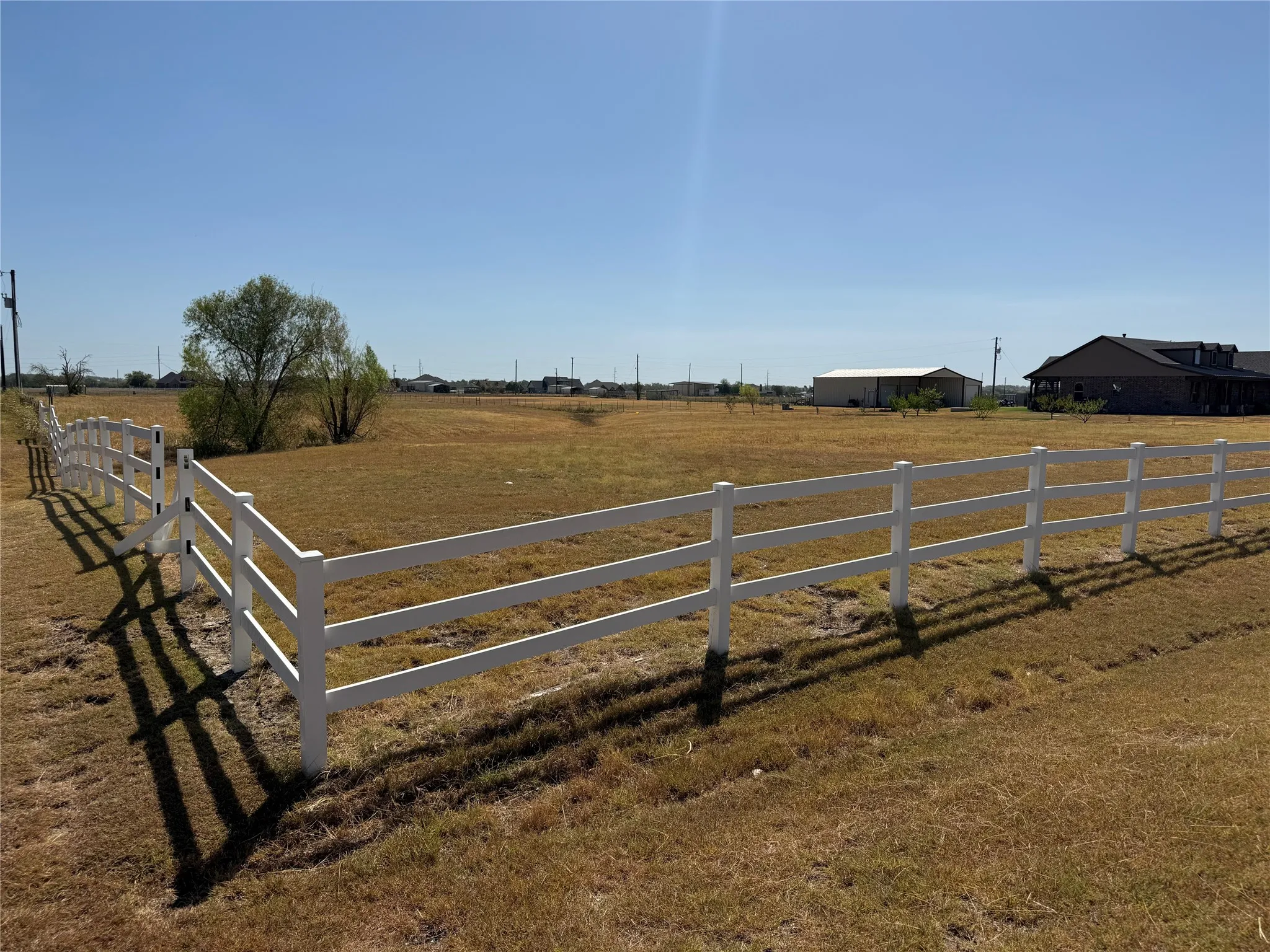 Expansive open land with a white three-rail fence