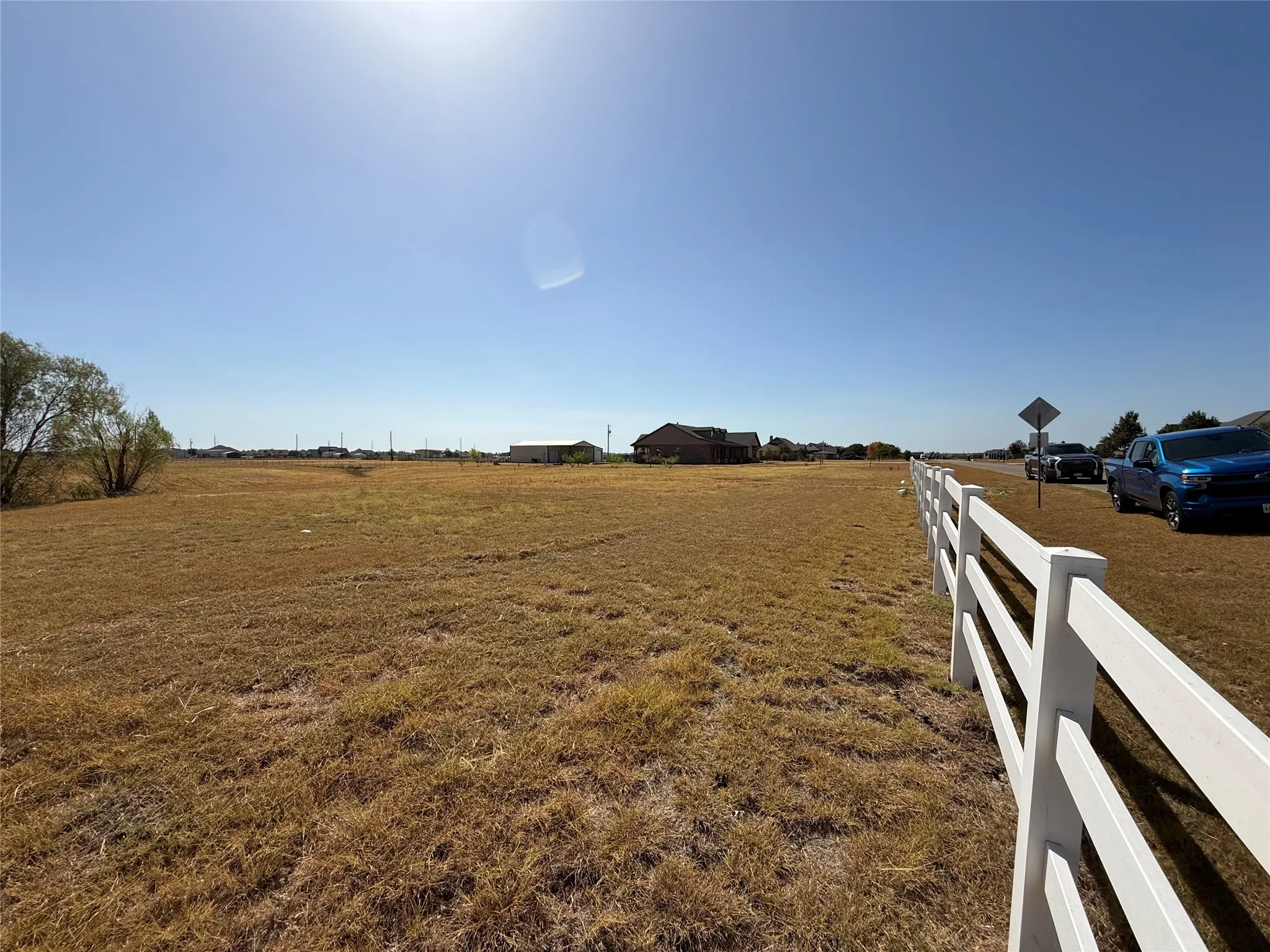 Expansive open land featuring a white split-rail fence, clear blue sky, and distant structures
