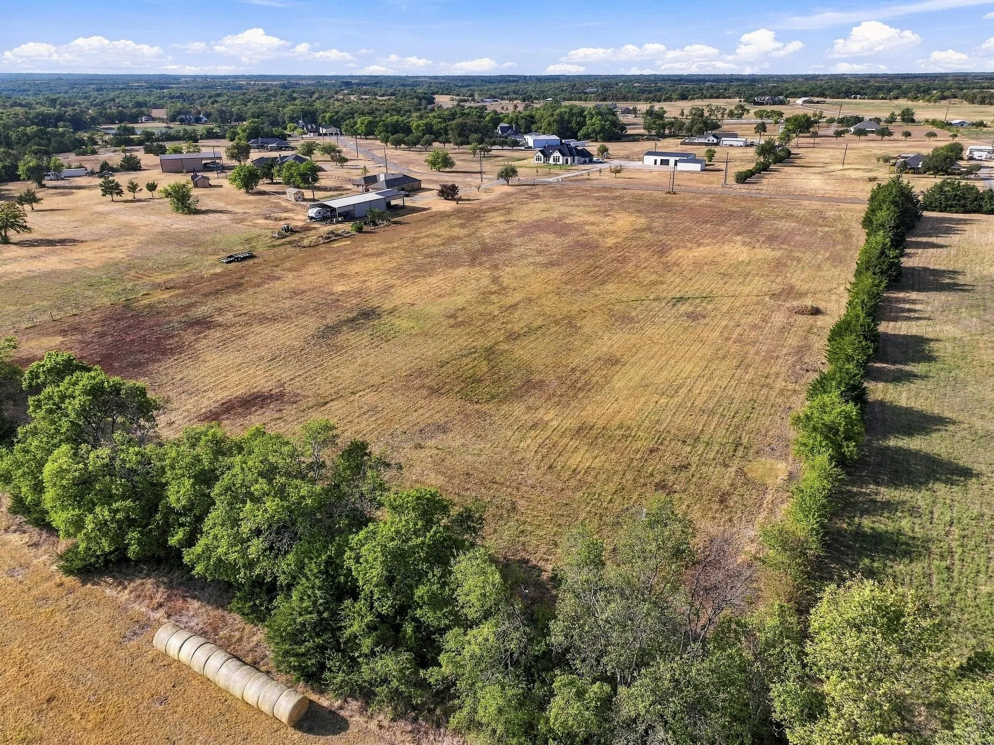 Expansive rural landscape featuring a cleared field, scattered mature trees, and distant structures