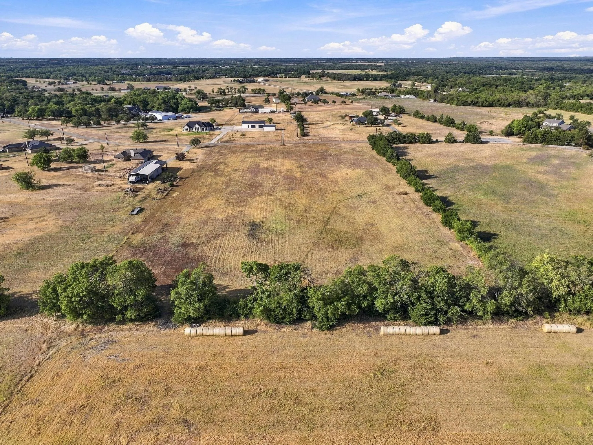 Expansive agricultural landscape featuring open fields and distant residential structures