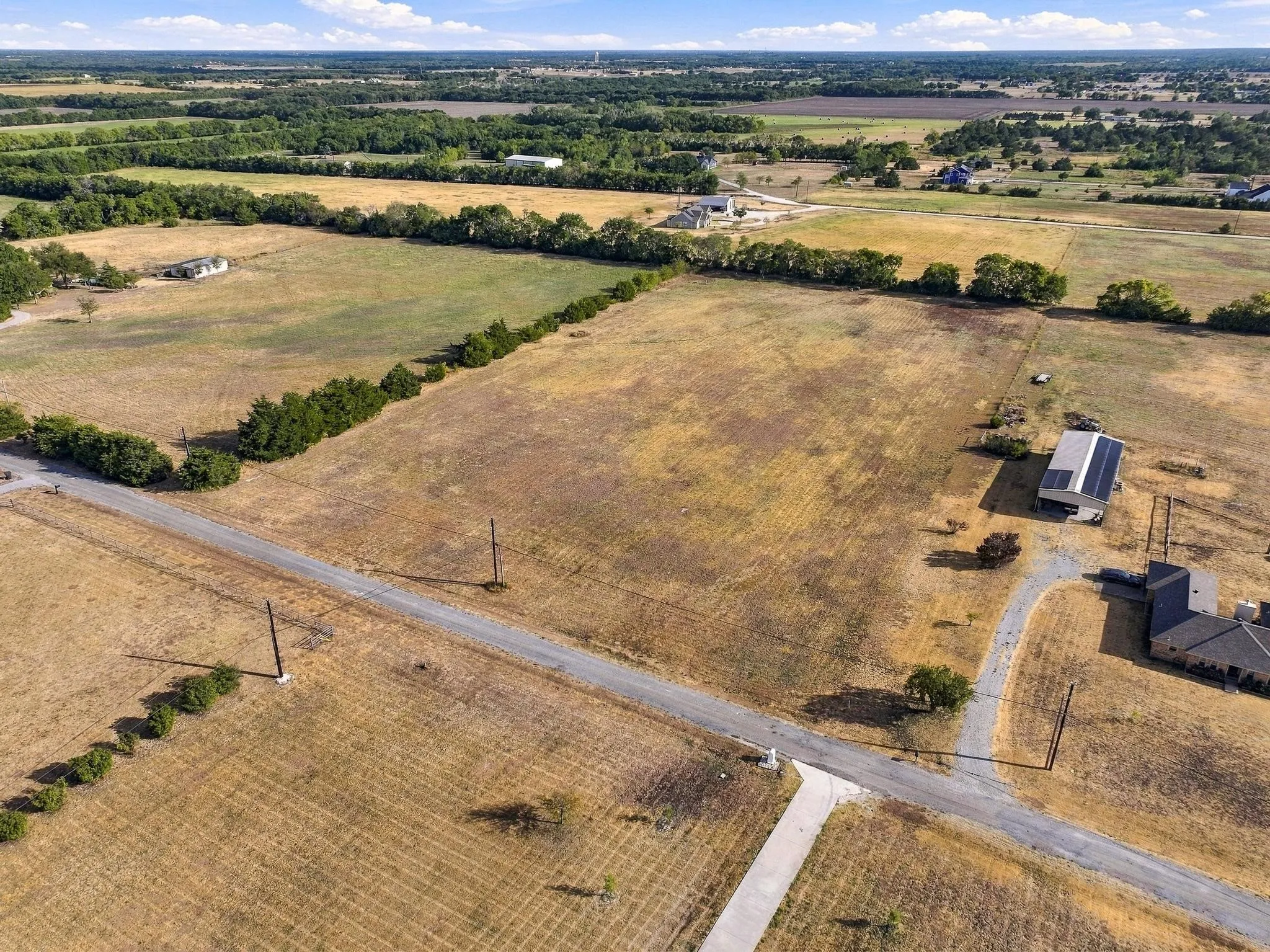 Expansive rural landscape featuring a paved road, scattered trees, and distant structures