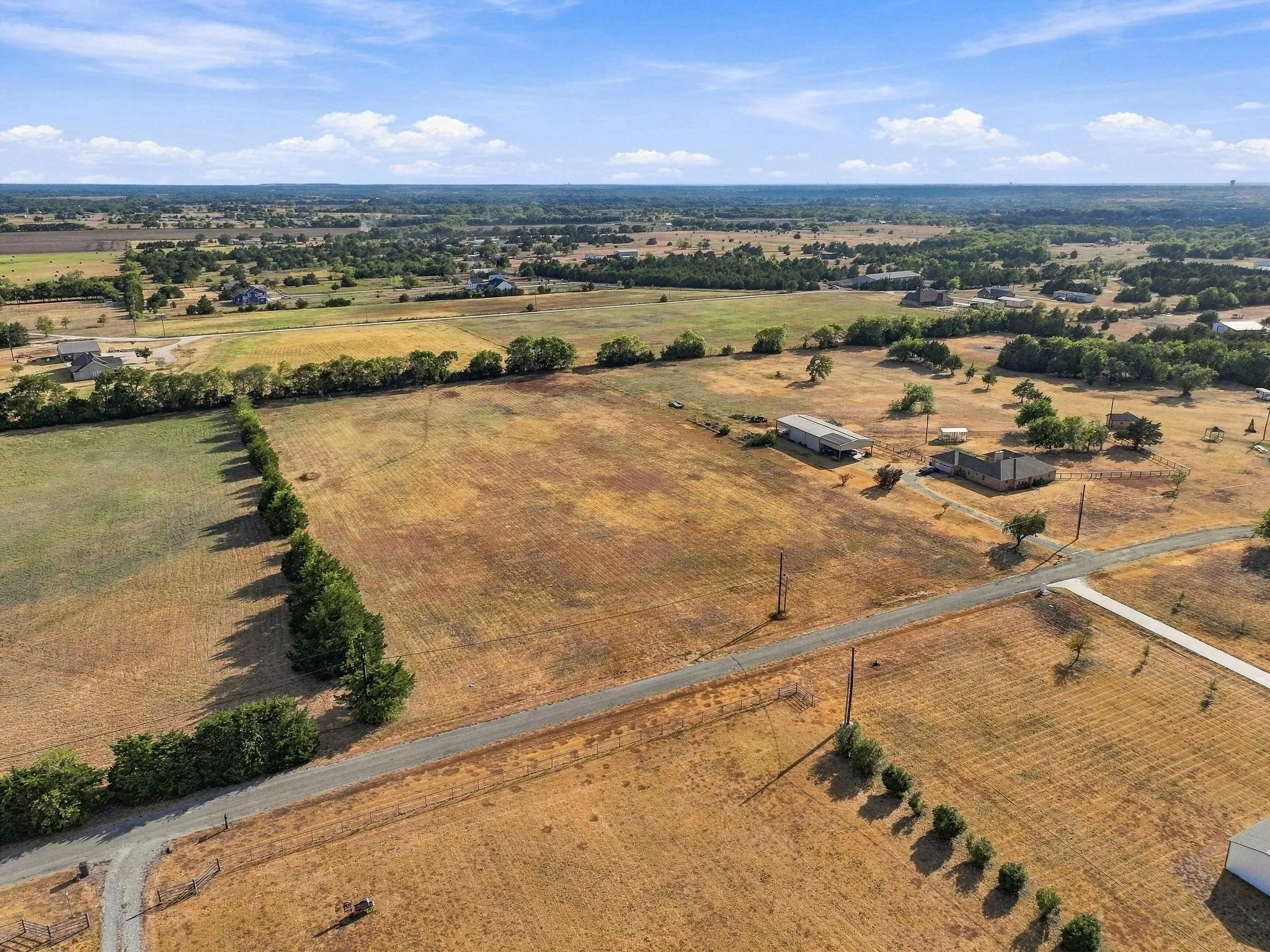 Expansive rural landscape featuring a single-story residence, a large outbuilding with an extended covered area, and a network of paved and unpaved roads