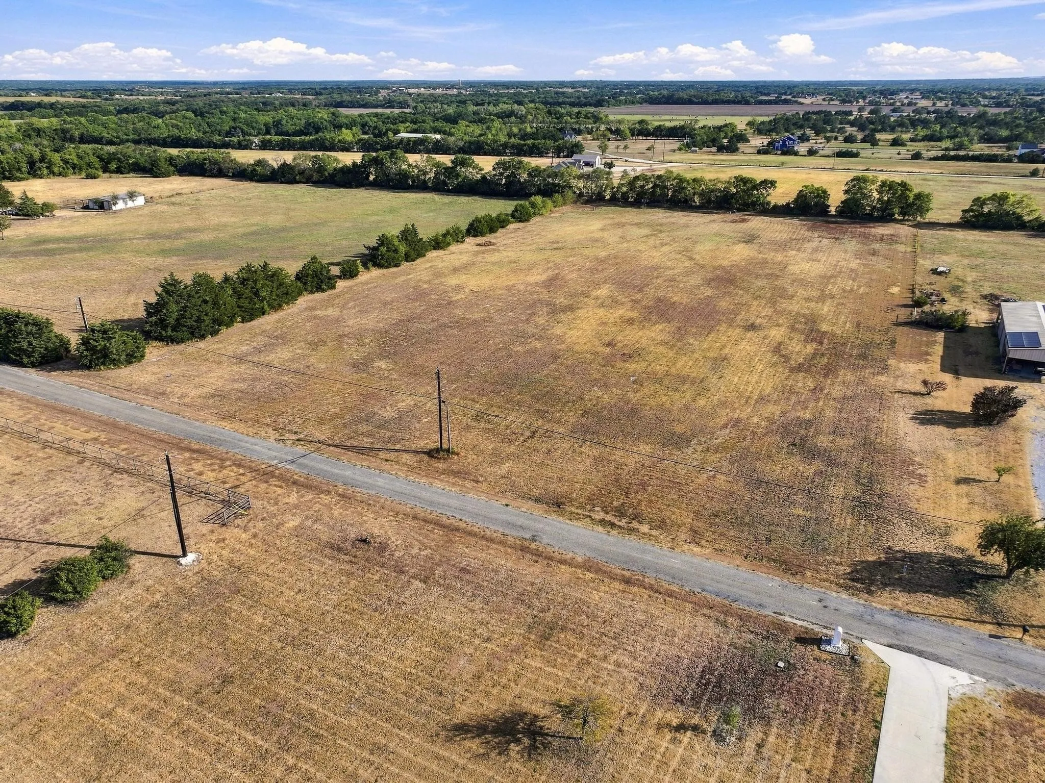 Expansive open land with a gravel road and mature trees bordering the perimeter