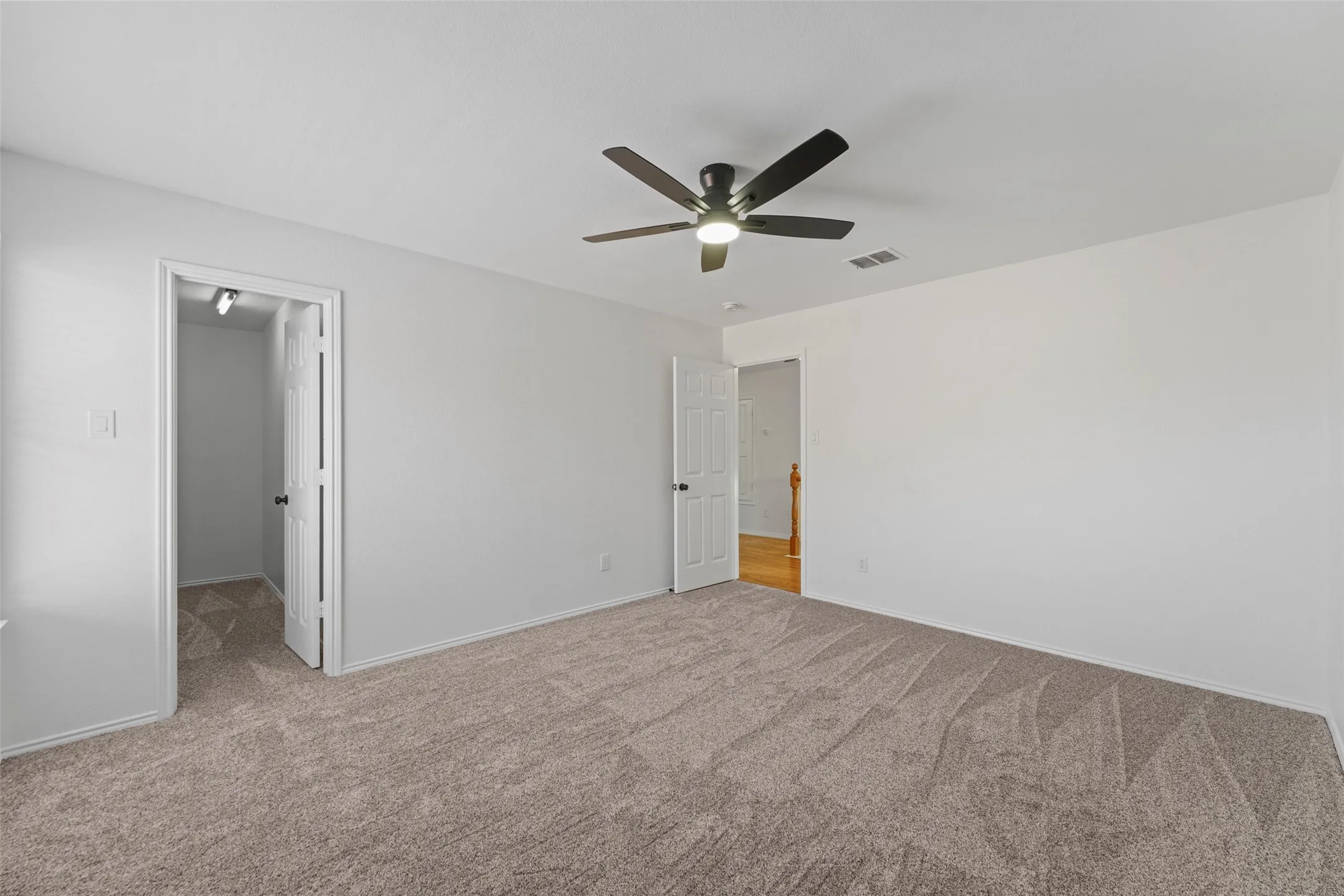 Spacious room with plush carpeting, neutral wall finishes, and a ceiling fan with integrated lighting