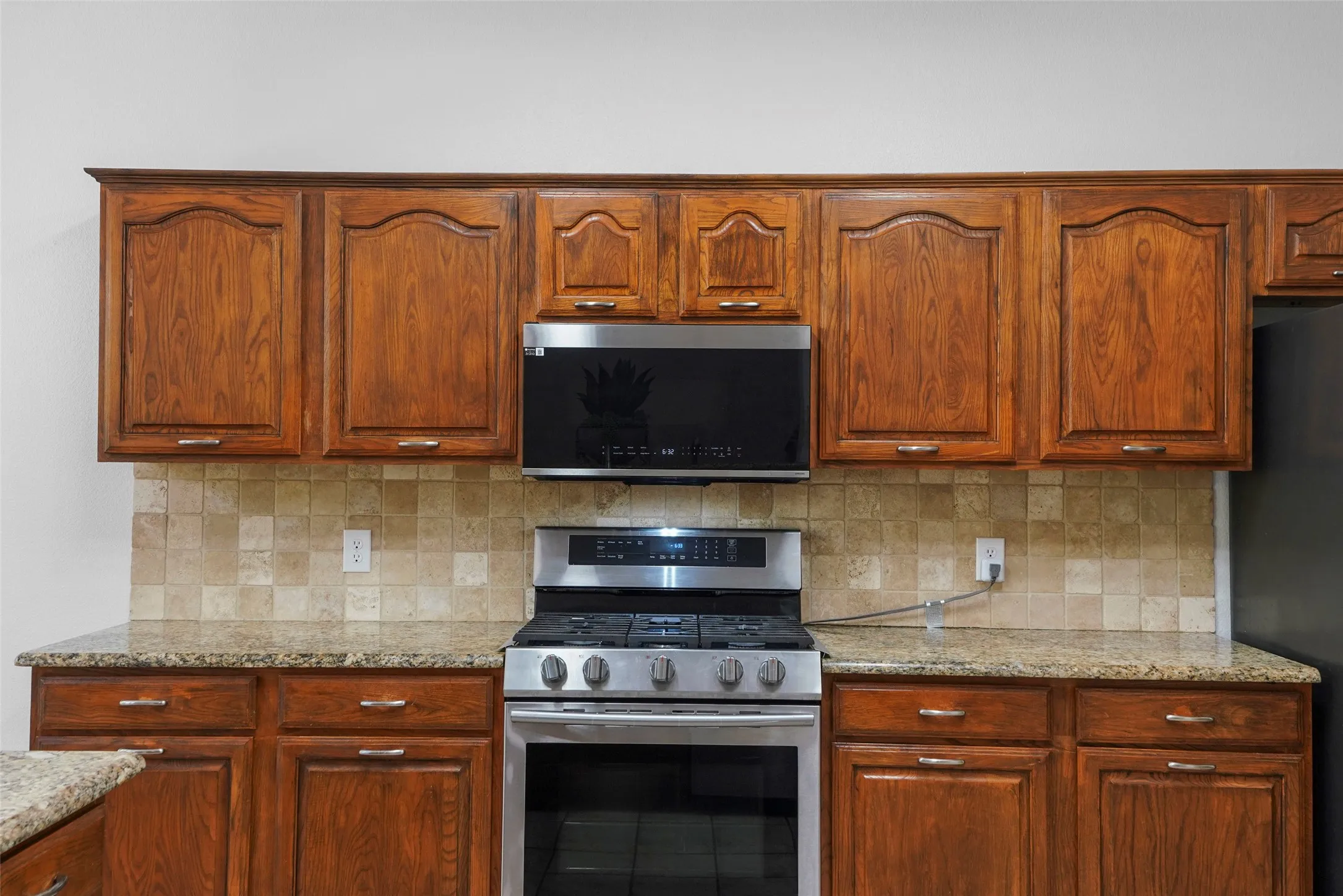 Wood cabinetry with arched panel doors, stainless steel appliance package, granite-style countertops, and a tiled backsplash
