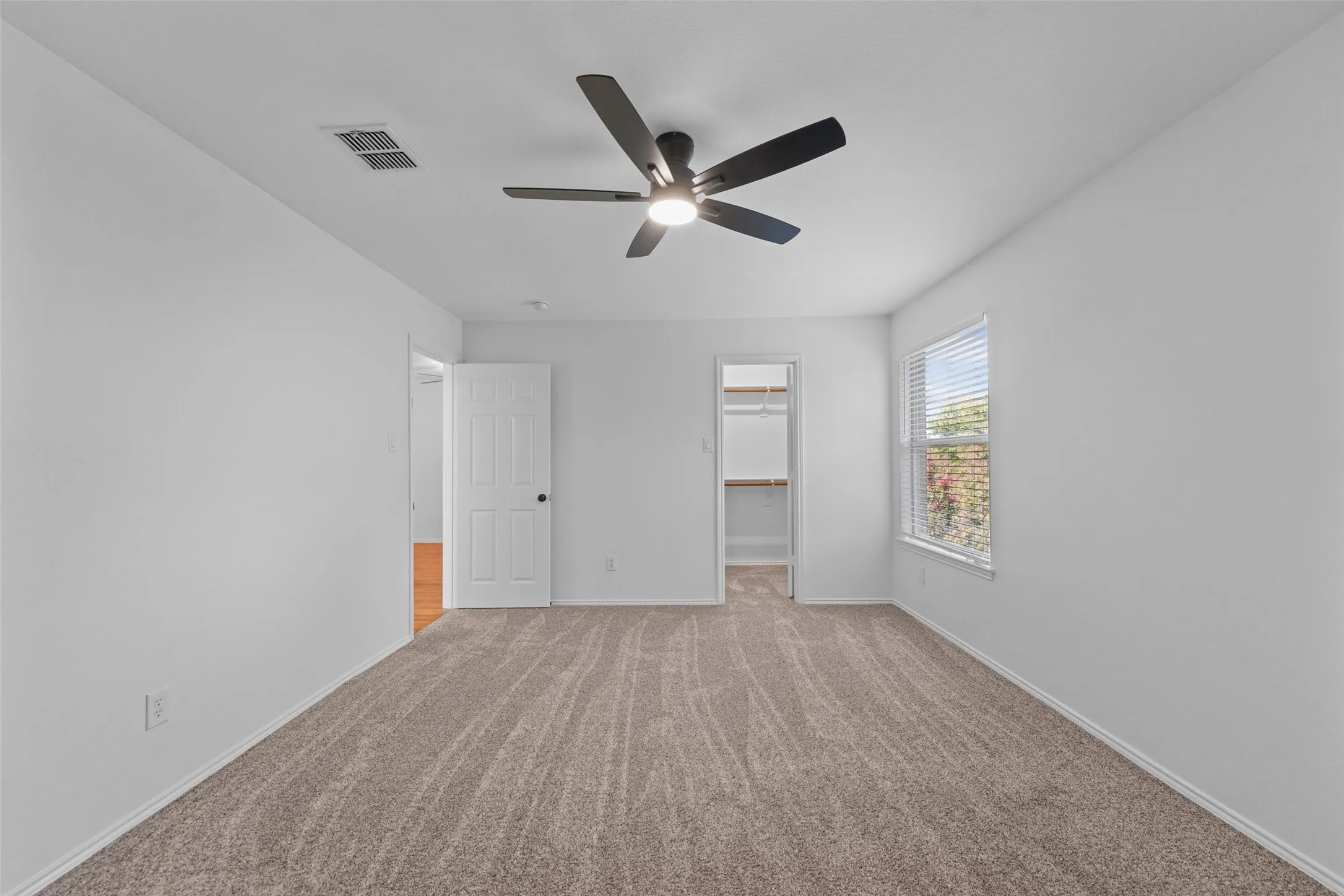 Bright, open bedroom featuring neutral wall finishes, plush wood-finish flooring, recessed ceiling lighting, and a modern ceiling fan with integrated light fixture