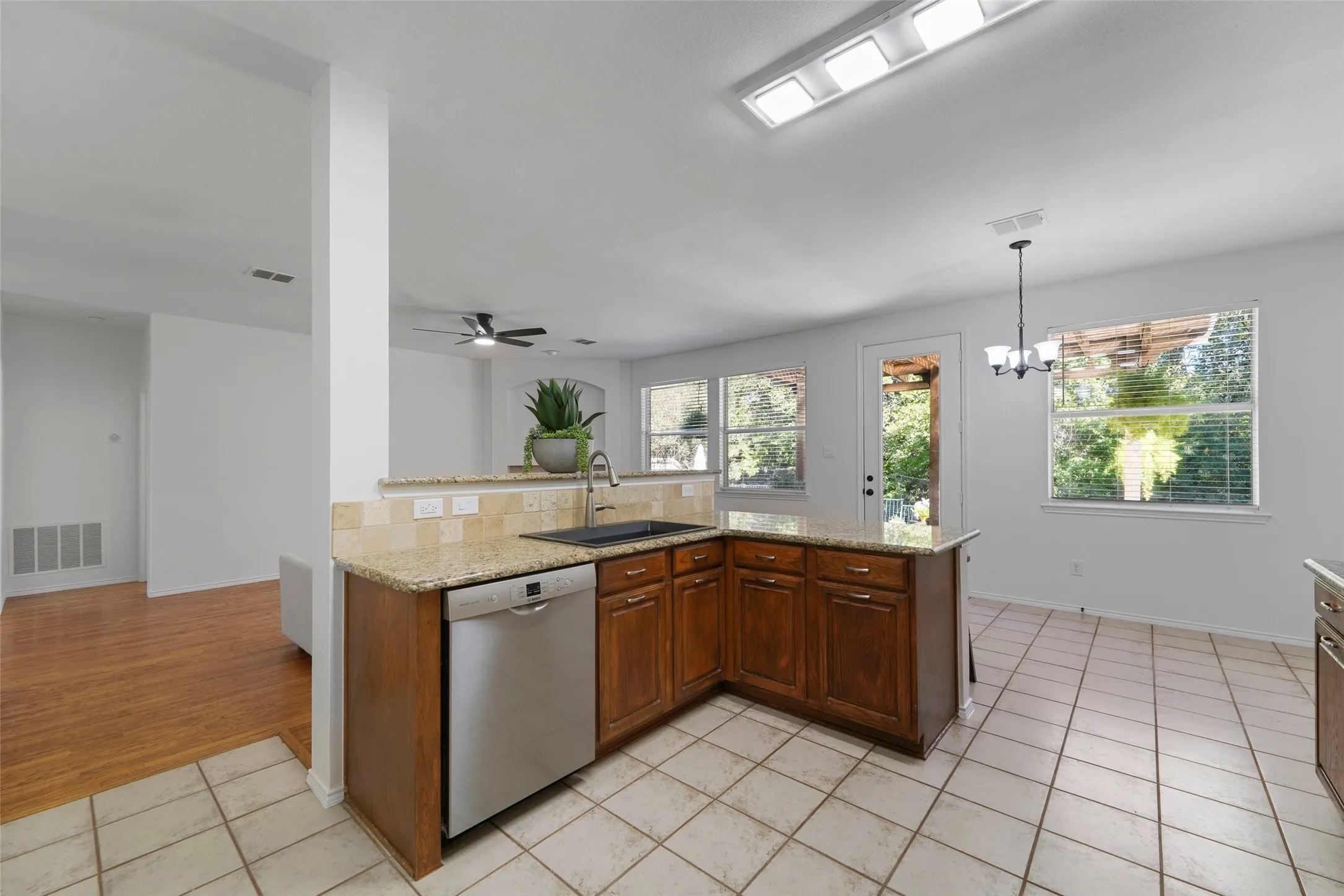 Kitchen featuring granite countertops, wood-finish cabinetry, a stainless steel dishwasher, and tile flooring