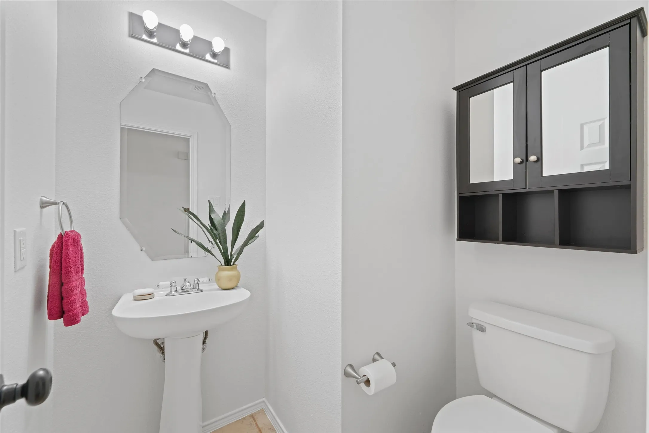 Pedestal sink with chrome fixtures, octagonal mirror, wall-mounted light fixture, and dark wood-finish medicine cabinet with open shelving