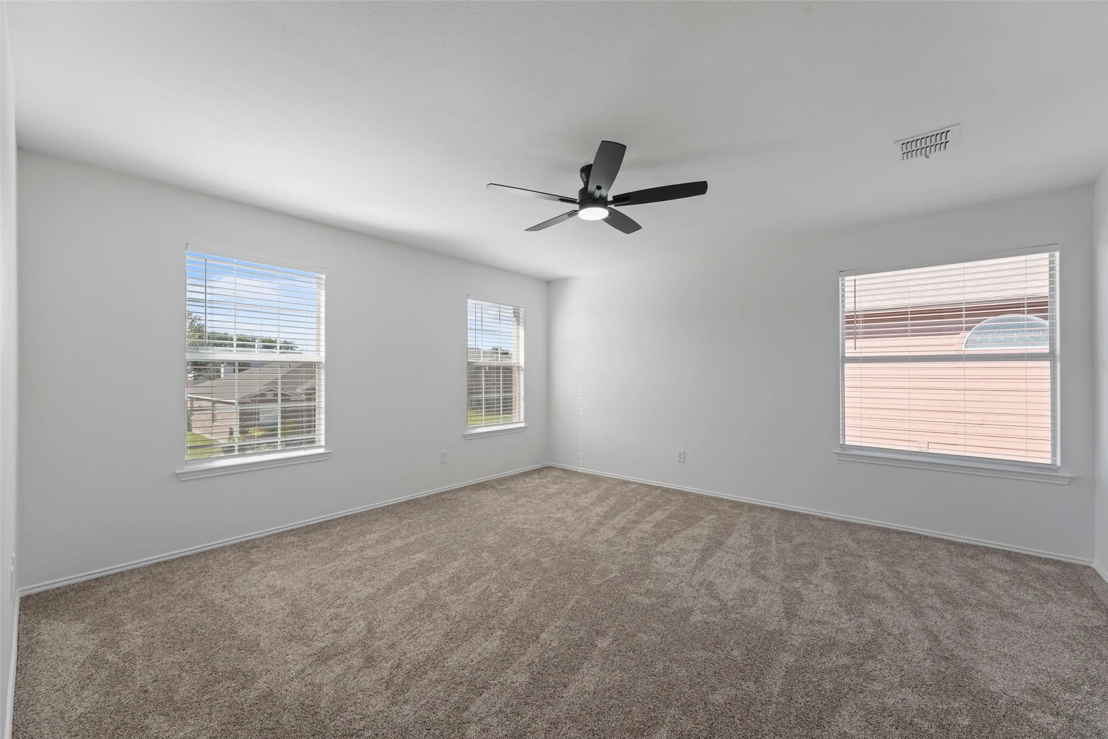 Bright interior with carpeted flooring, multiple windows, and a ceiling fan with integrated lighting