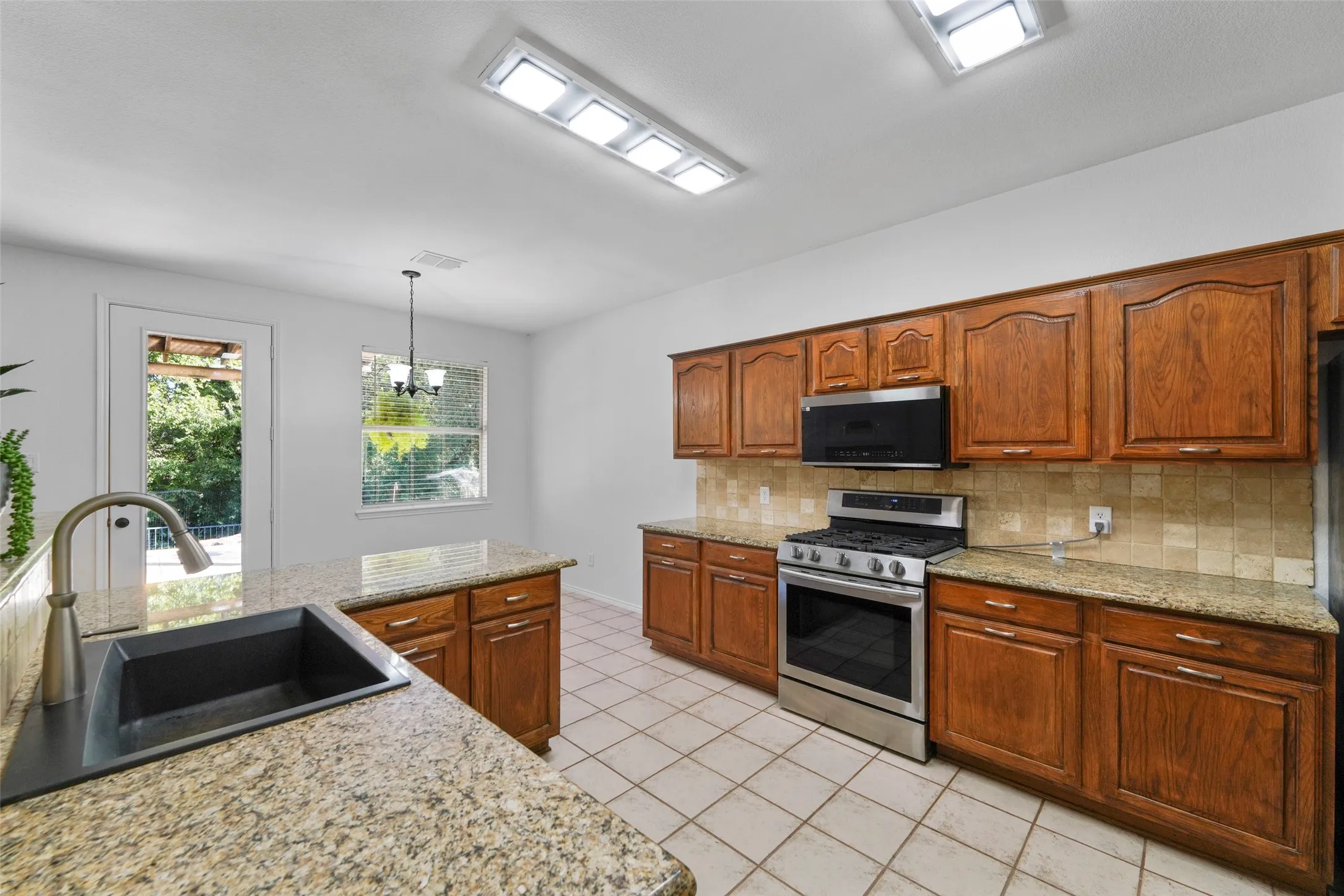 Kitchen featuring granite countertops, wood cabinetry, stainless steel range and microwave, and tile flooring
