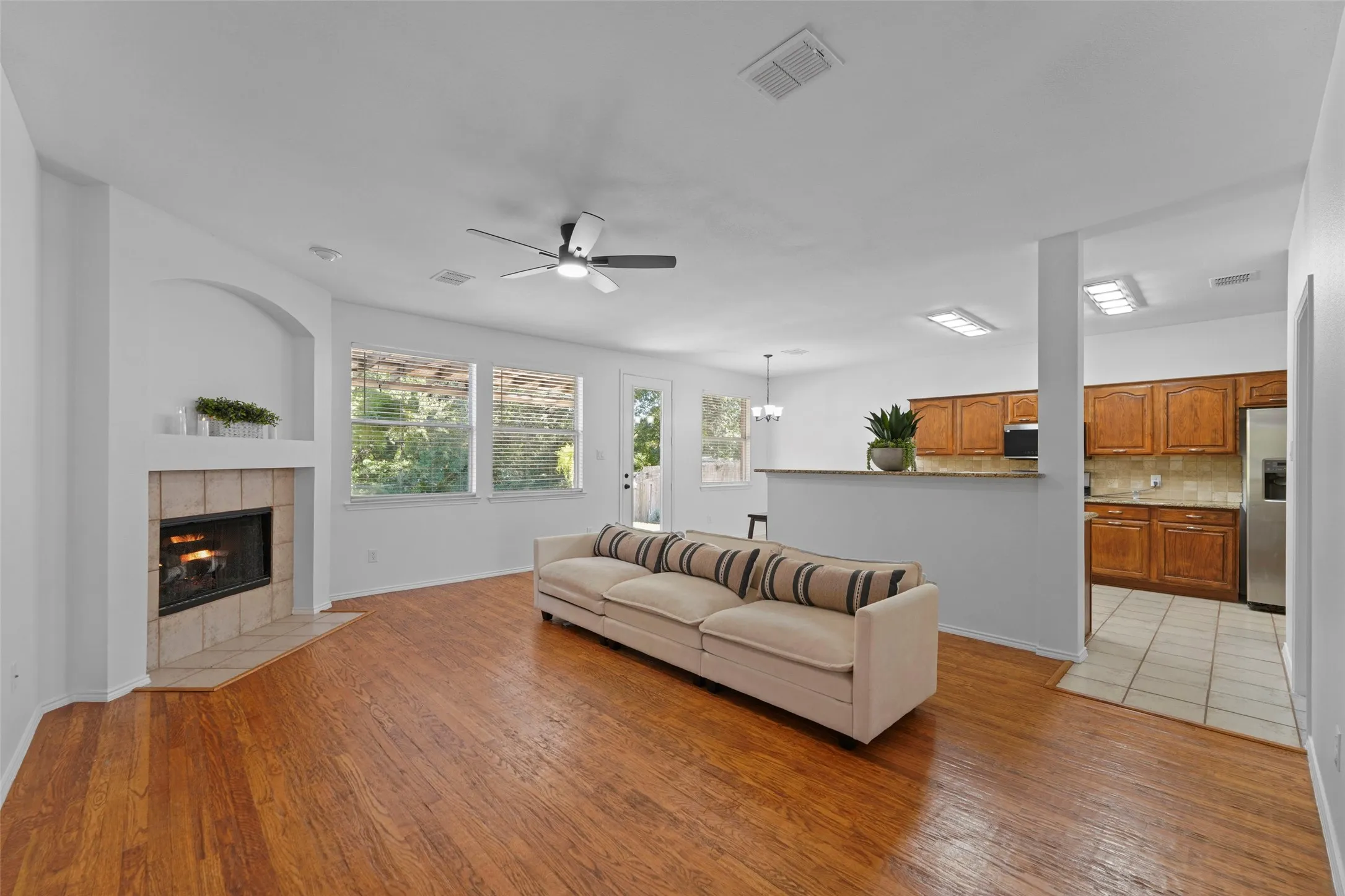 Wood-finish flooring, tiled fireplace with arched niche, ceiling fan, and updated kitchen with wood cabinetry and stainless steel appliances