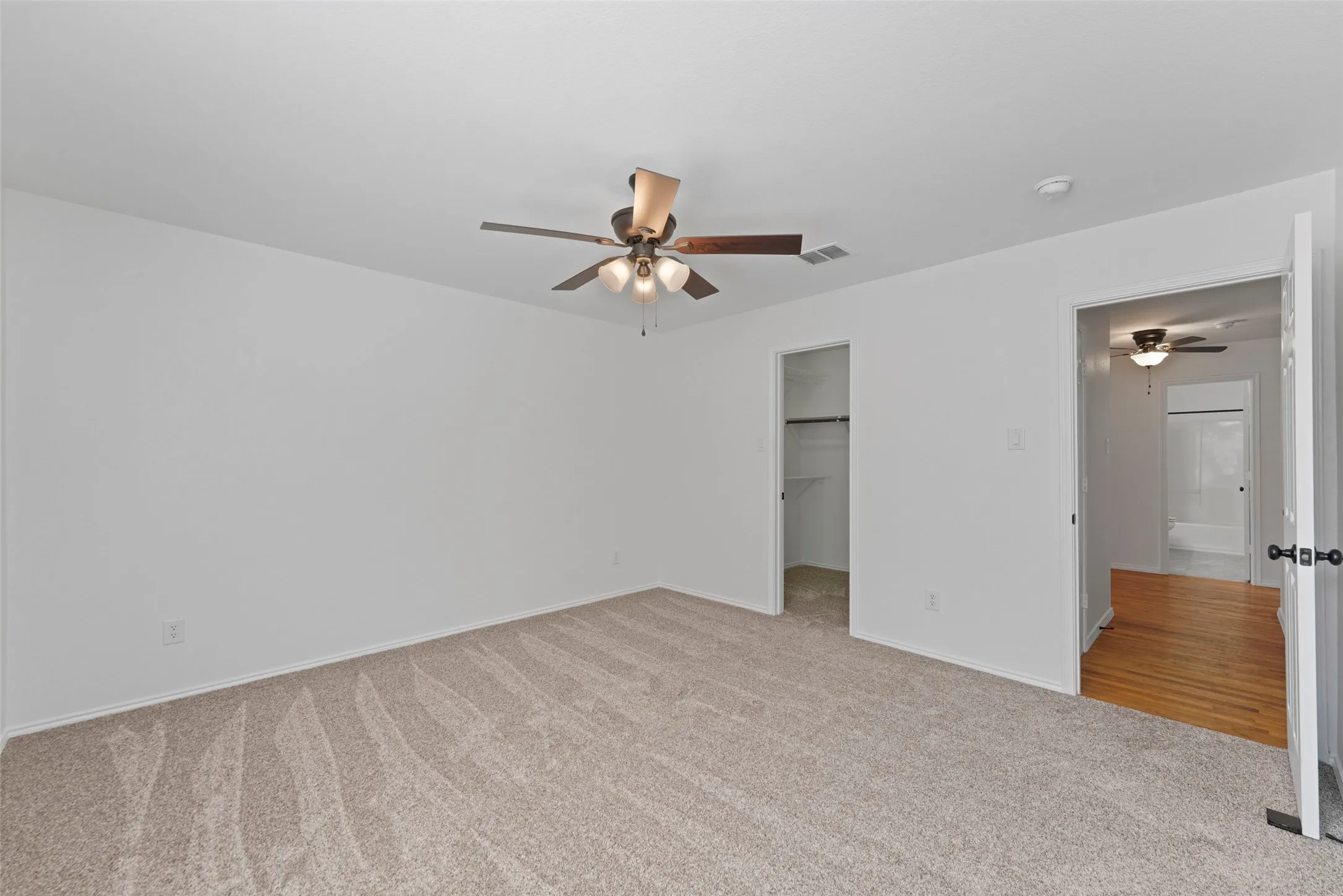 Carpeted room with a ceiling fan, a closet with built-in shelving, and a doorway leading to a hall with wood-finish flooring