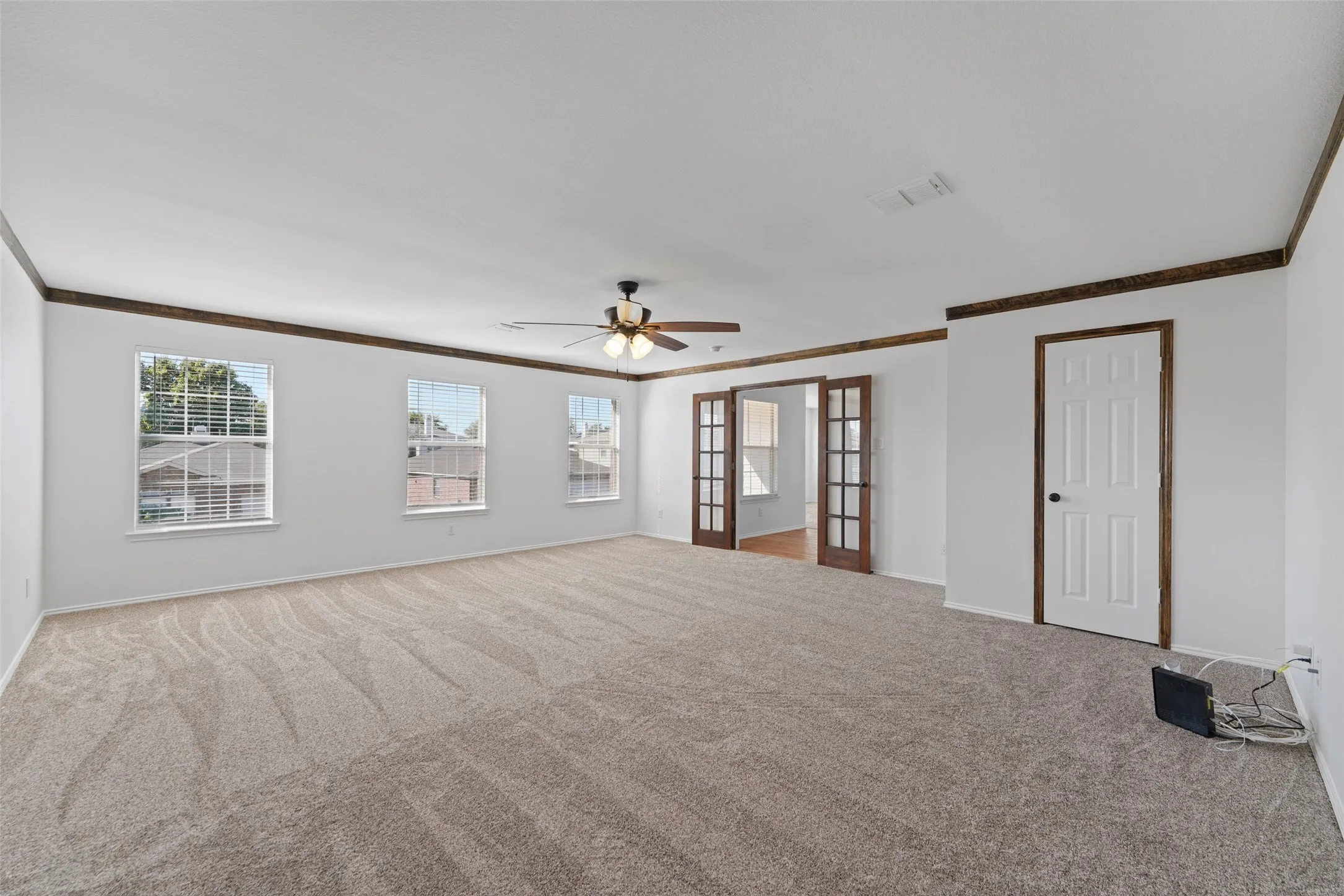 Spacious room with plush carpet flooring, multiple windows, a ceiling fan, and French doors leading to an additional space