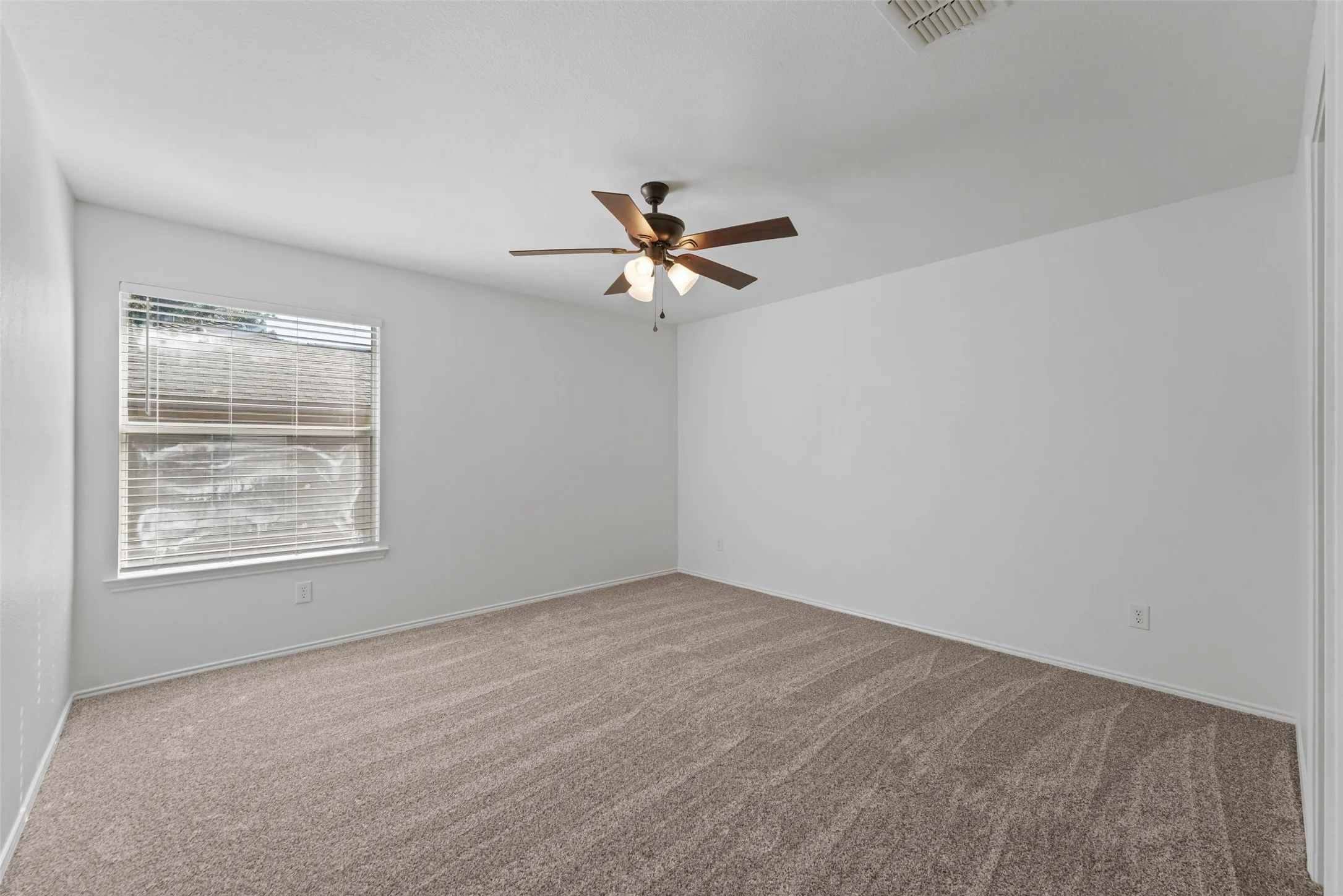 Spacious interior featuring neutral carpet, a ceiling fan with integrated lighting, and a window with blinds