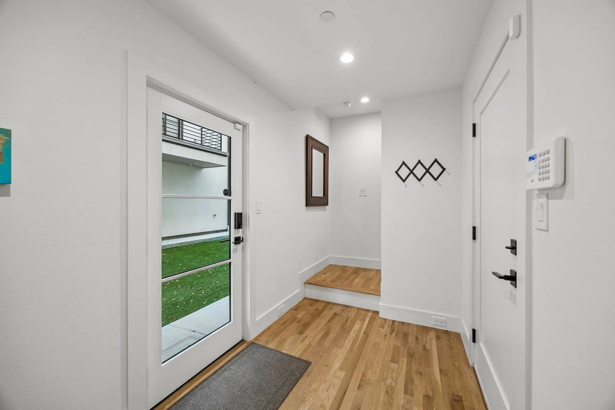 Doorway leading to the shared greenway with turf, complemented by oak wood-finished flooring and recessed lighting that enhance the clean, modern feel of the interior.