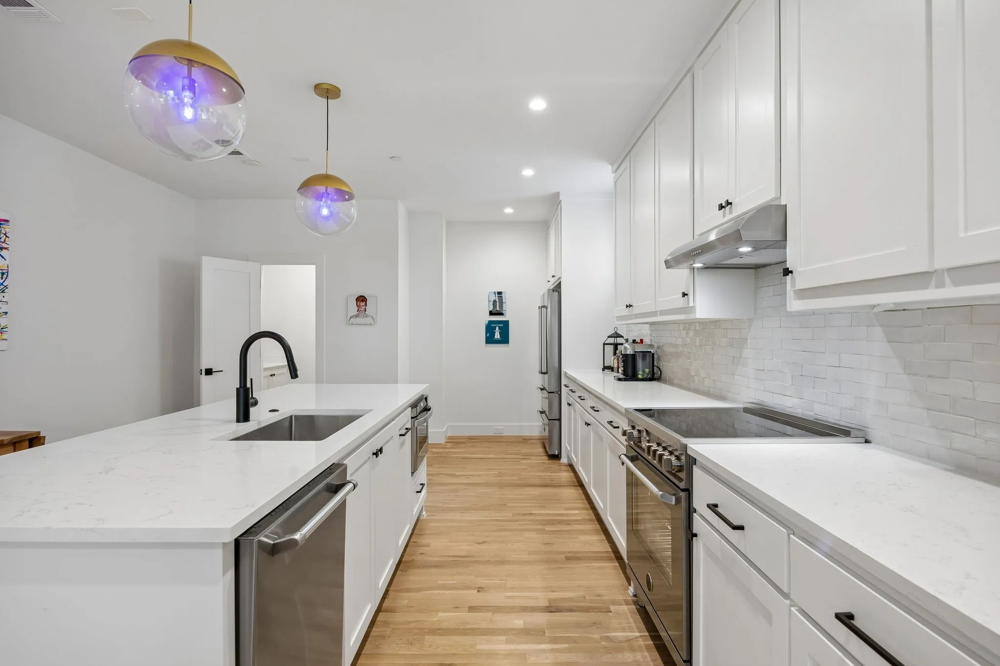Chef inspired kitchen featuring high end Bertazzoni appliances, stainless steel finishes, light oak wood flooring, and crisp white shaker style cabinetry, all complemented by light stone countertops and a spacious island with built in sink.