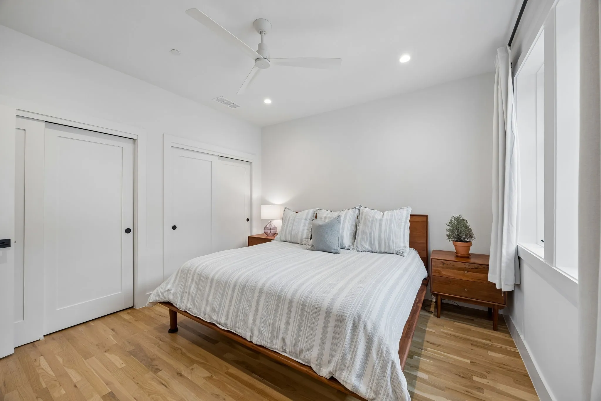 Bedroom with two closets, light oak wood flooring, recessed lighting, and a ceiling fan.