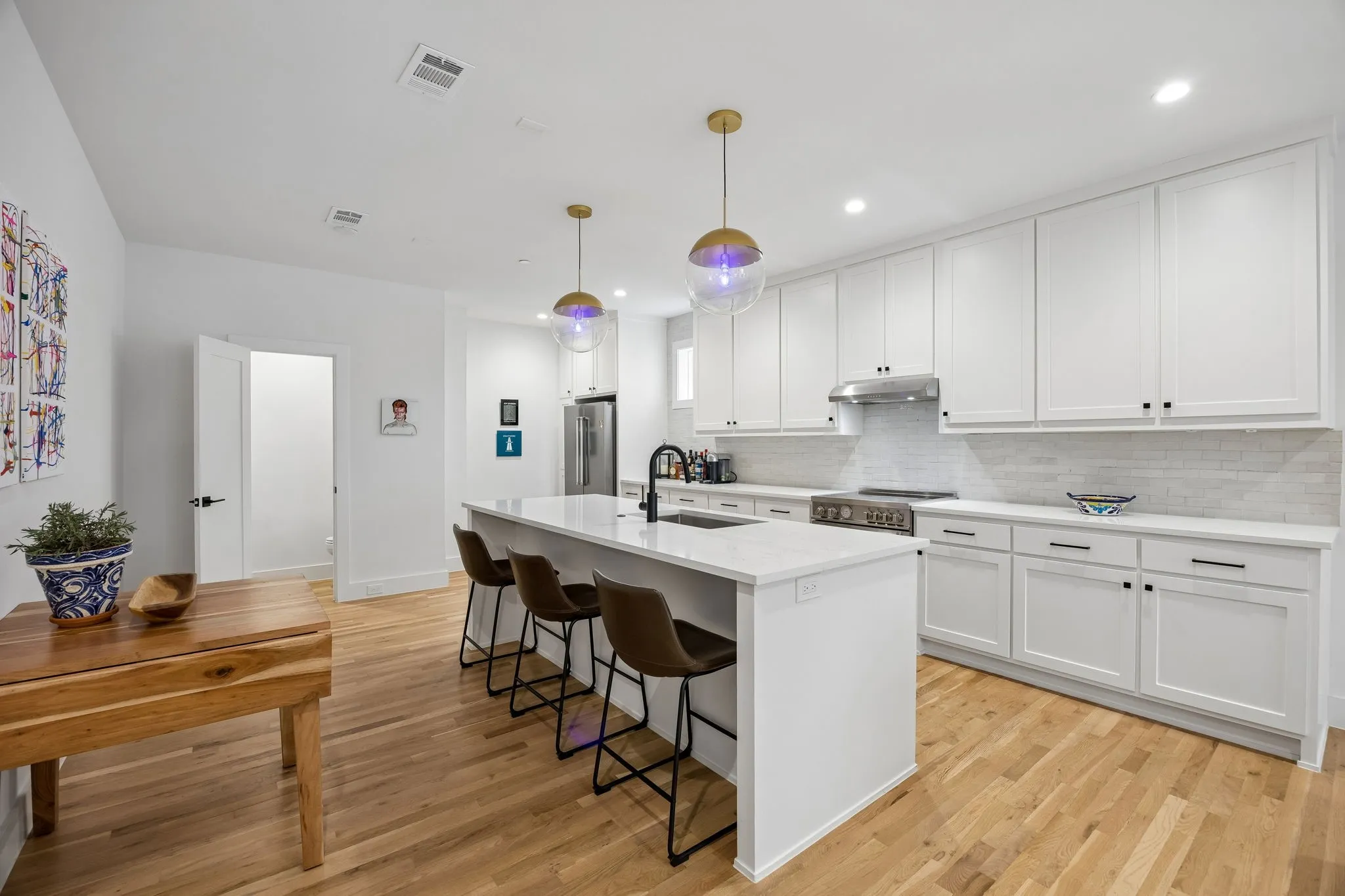 Open kitchen with island, white cabinets, stainless steel Bertazzoni appliances, and hanging light fixtures.