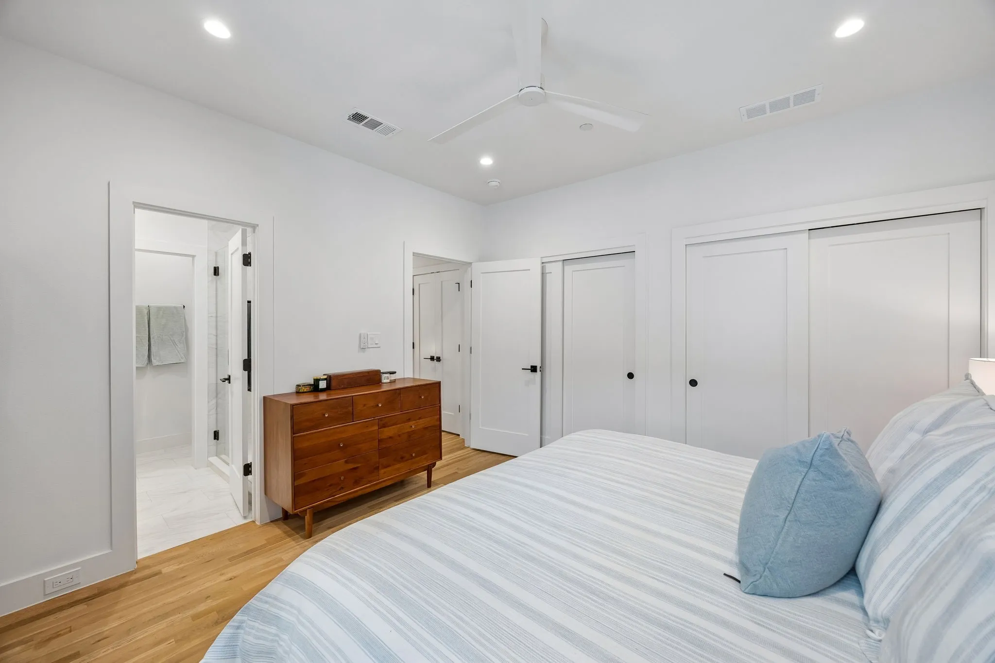 Bedroom with light oak wood floors, two closets, a ceiling fan, and recessed lighting with en-suite bathroom, dual sinks and walk-in shower