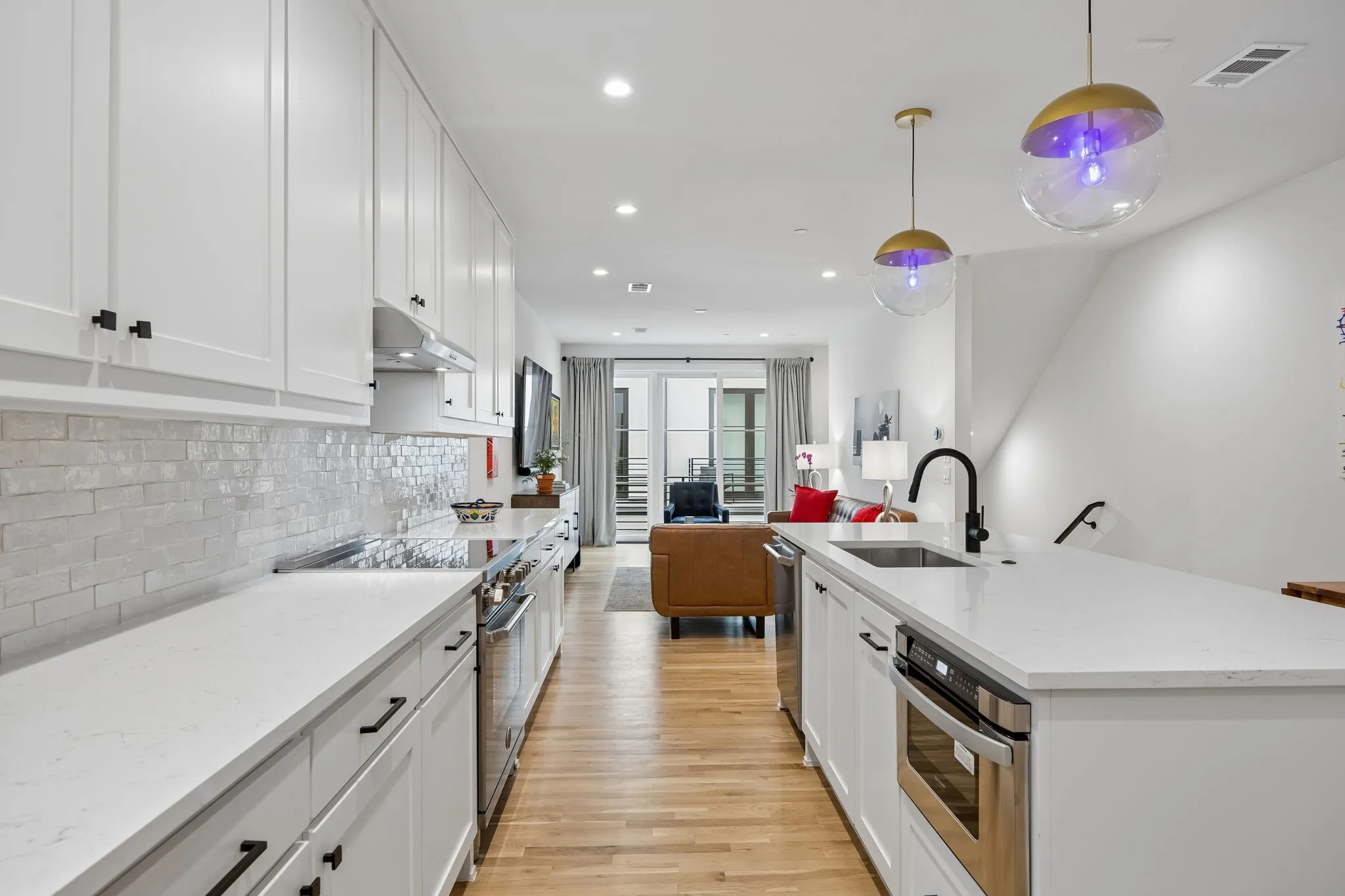Modern kitchen featuring white shaker cabinetry, stainless steel appliances, a white subway tile backsplash, light wood-finish flooring, and pendant lighting