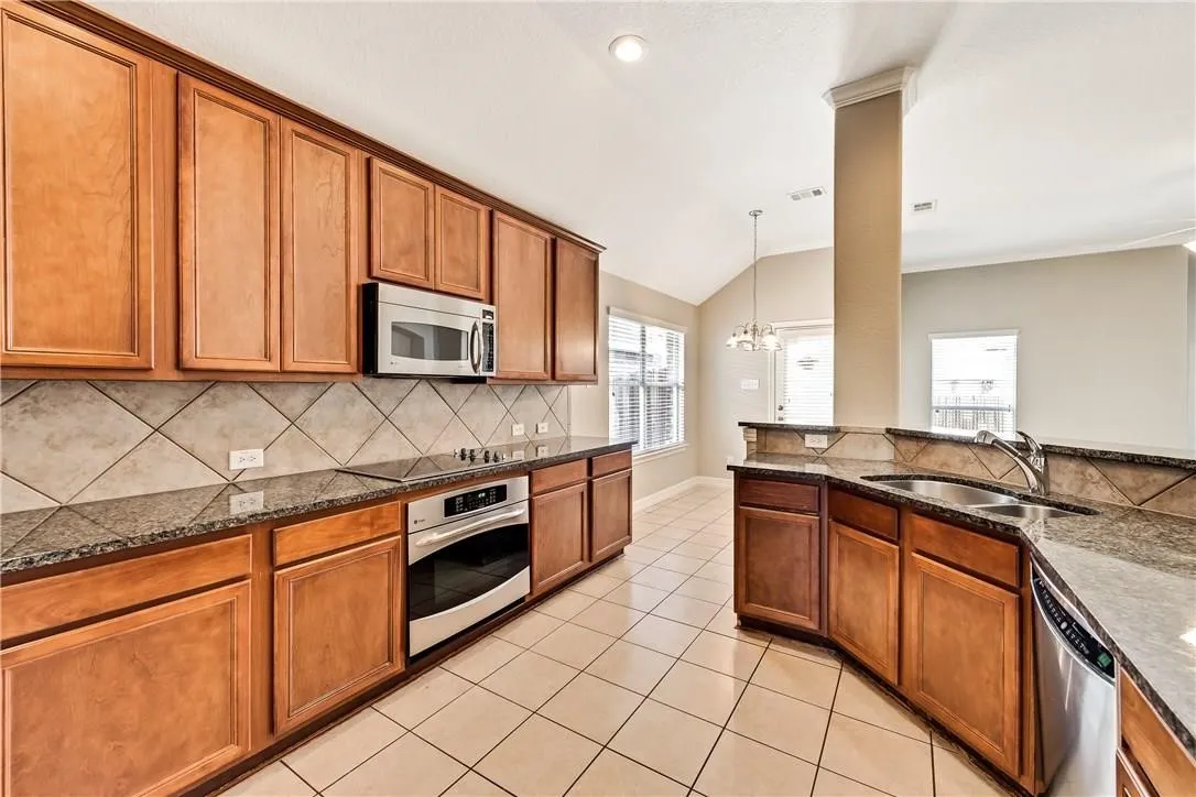 Kitchen featuring wood cabinetry, stainless steel appliances, granite countertops, and a tiled backsplash
