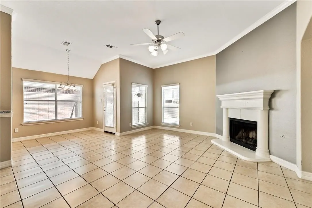 Spacious living area featuring tile flooring, vaulted ceilings, a fireplace with a white mantel, and multiple windows with blinds