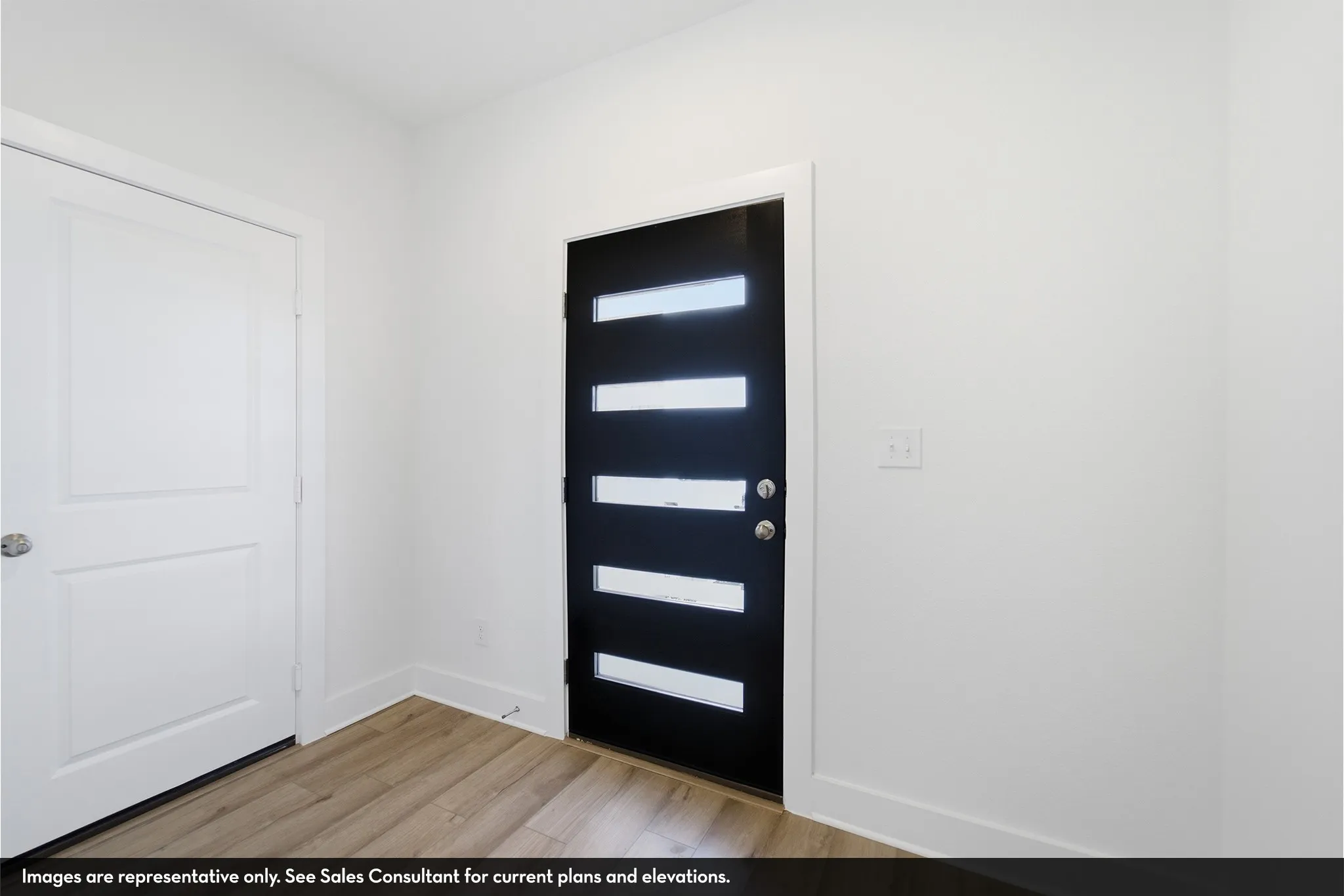 Modern black entry door with frosted glass inserts, wood-finish flooring, and white wall finishes