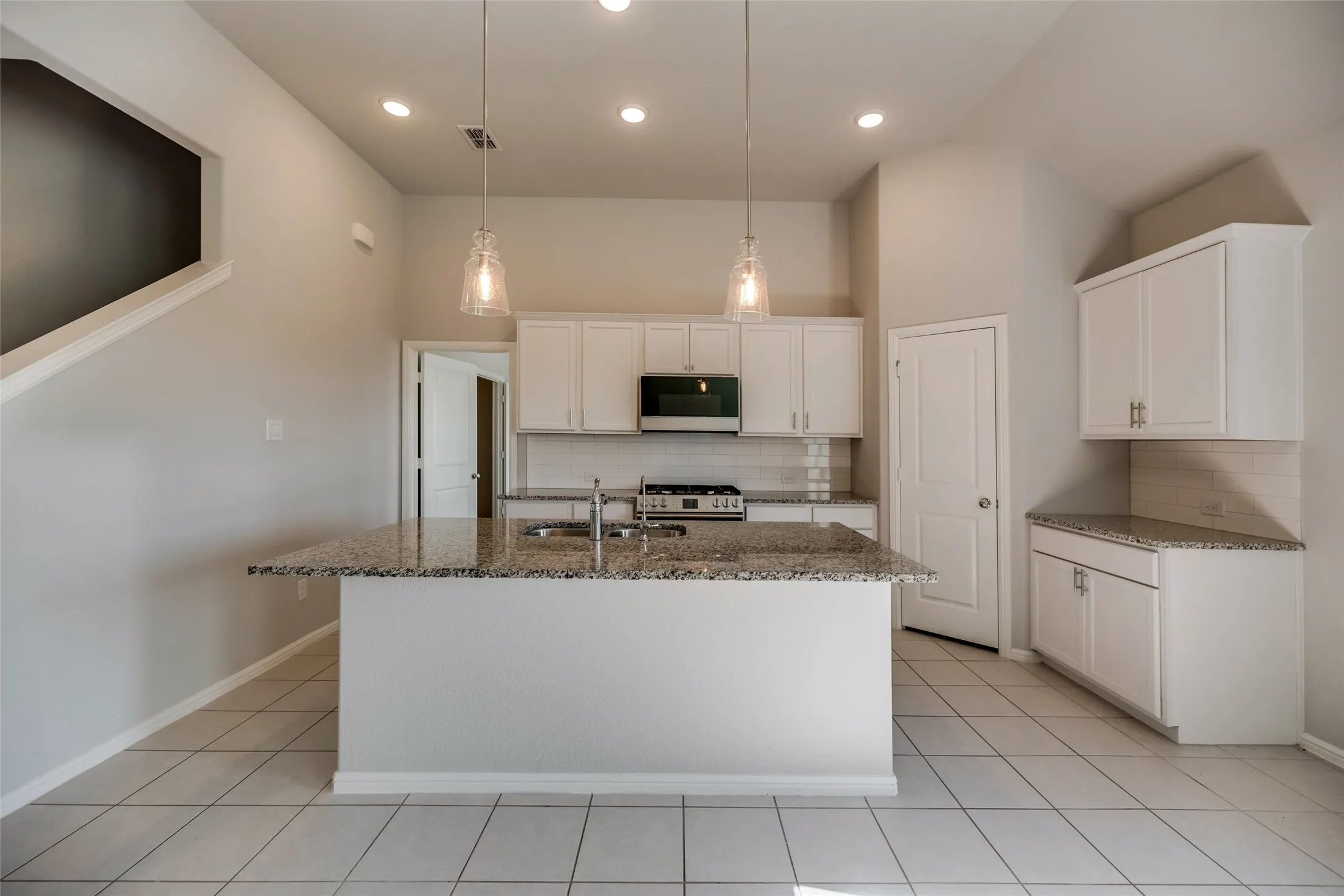 Kitchen featuring an island with a sink, stainless steel appliances, white cabinetry, pendant lighting, and tile flooring